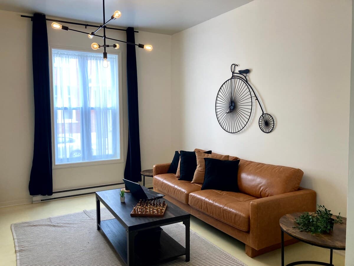Bright and stylish living room with mid-century charm, leather sofa, smart TV, chic decor, and a cozy vibe—perfect for relaxing, working remotely, or enjoying a game night. Air-conditioned and filled with natural light for year-round comfort.