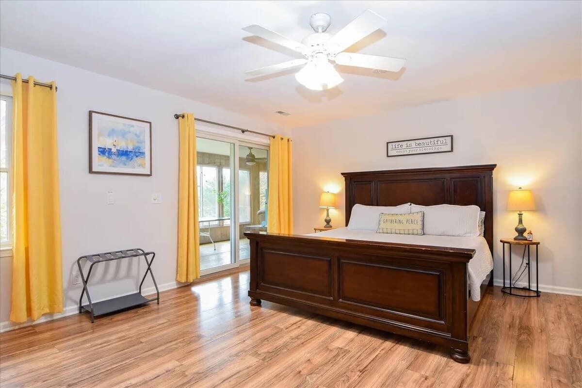Spacious primary king suite with walk-in closet, flat-screen TV, and private sunroom access overlooking the lake.king bed, walk-in closet, primary suite, sunroom access, flat-screen TV, luxury lvp  floors, natural light, lake house master bedroom