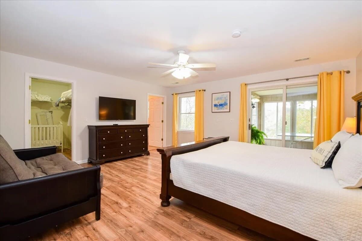 Spacious primary king suite with walk-in closet, flat-screen TV, and private sunroom access overlooking the lake.ing bed, walk-in closet, primary suite, sunroom access, flat-screen TV, luxury LVP floors, natural light, lake house master bedroom.