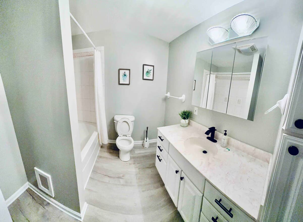 Very Spacious full guest bath with tub & shower — soak off the lake day. full bathroom, tub/shower combo, marble appearing vanity, matte black fixtures, medicine cabinet, gray plank floors, family-friendly, spa-inspired.