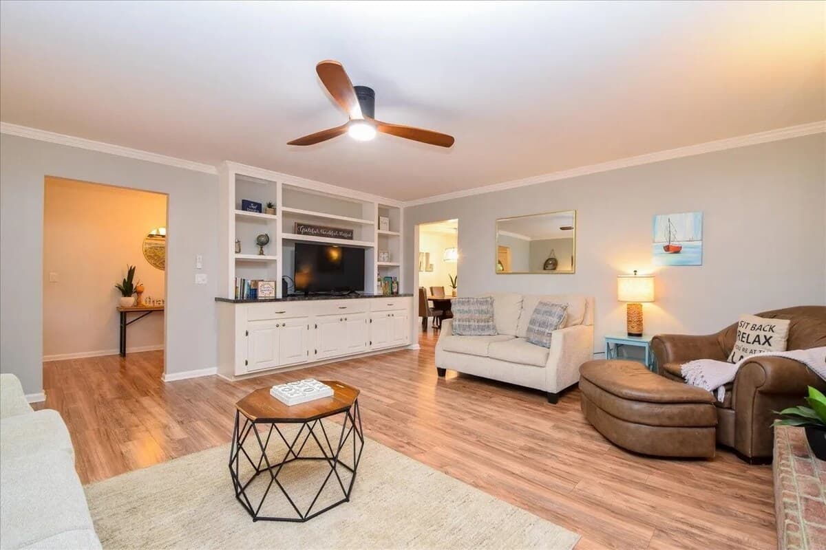 Open-concept living room — seats 6+ around a floor-to-ceiling brick fireplace. Flat-screen TV, built-in bookshelves, and flow to the kitchen — entertain everyone. 1 large couch, oversized chair and large love seat. 