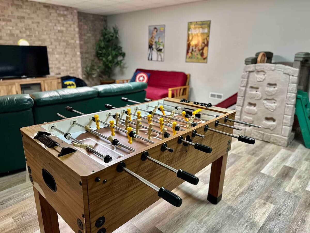 One giant lower-level fun zone — foosball, kids' play area, and TV lounge all in one open space.

Foosball table, open basement, game room + play area, multigenerational, family-friendly, kid-friendly, group hangout, lower-level fun zone.