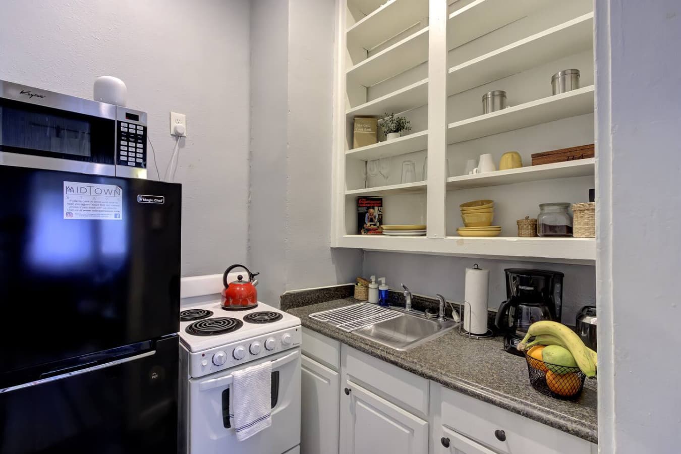 As you step into the compact kitchen, the vibe welcomes you with its clean, organized shelves and essentials like a coffee maker, ready to fuel your mornings.