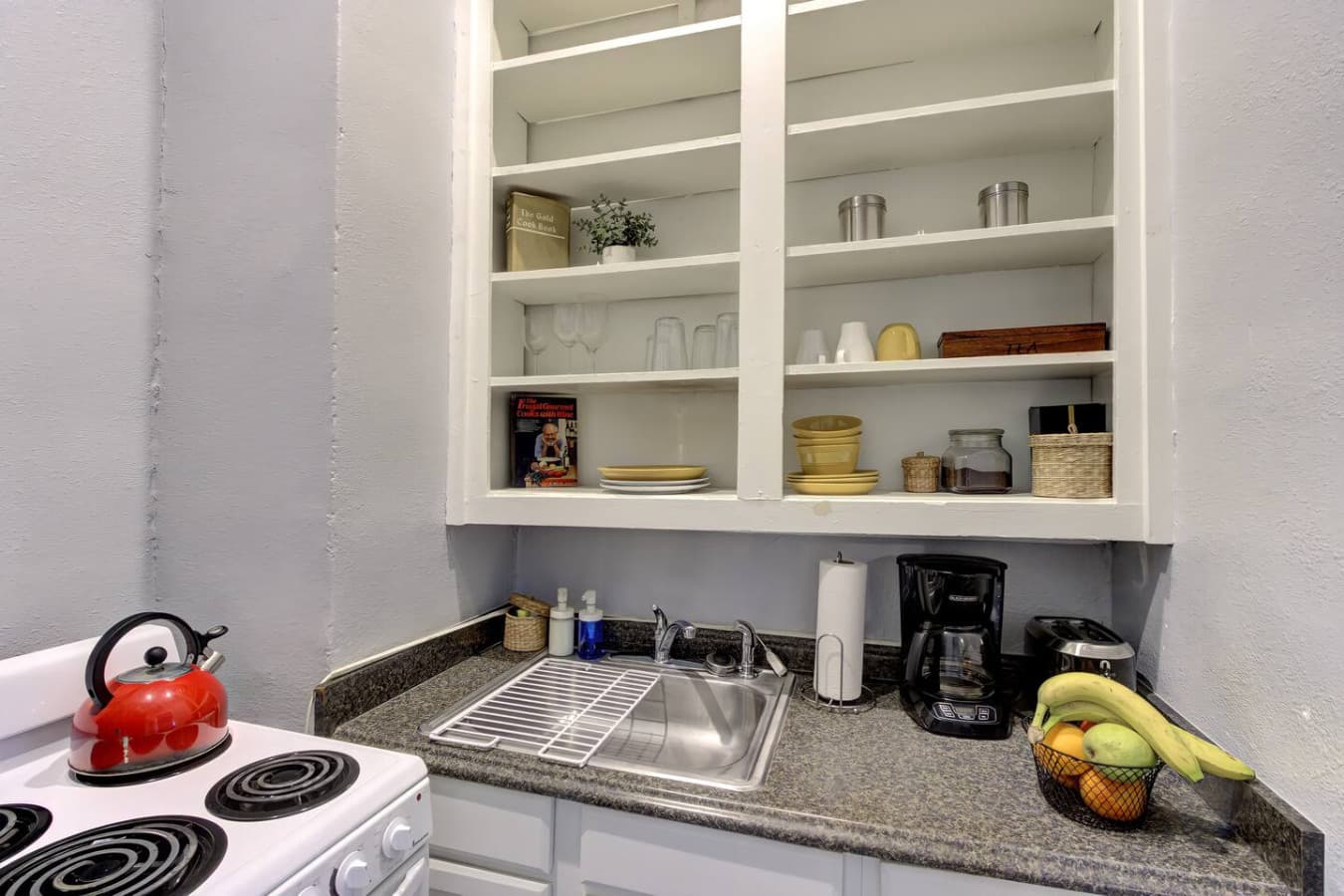 As you step into the compact kitchen, the vibe welcomes you with its clean, organized shelves and essentials like a coffee maker, ready to fuel your mornings.