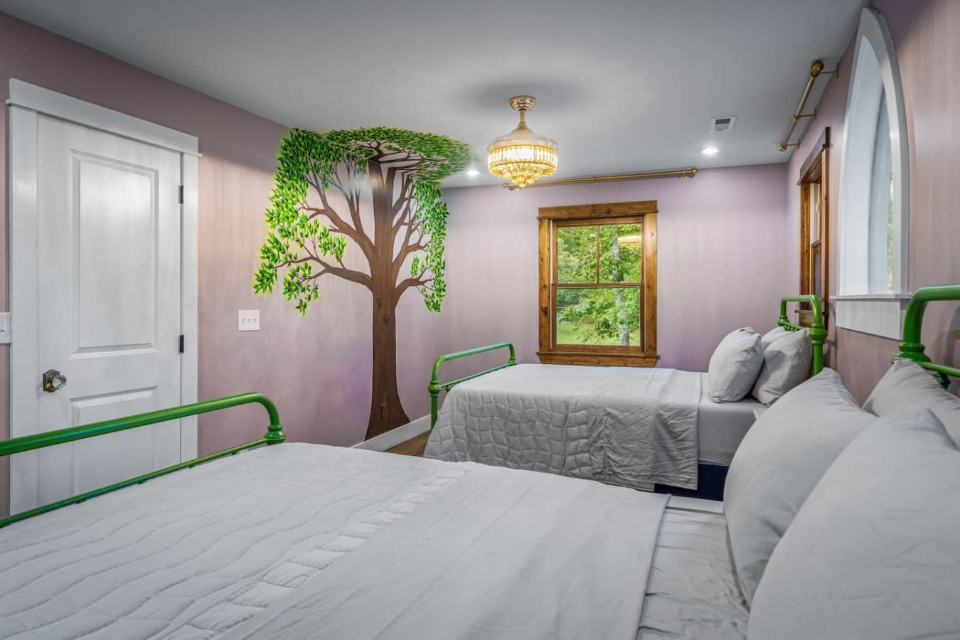 A vibrant room featuring two queen beds and whimsical tree murals, creating a peaceful, nature-inspired retreat.