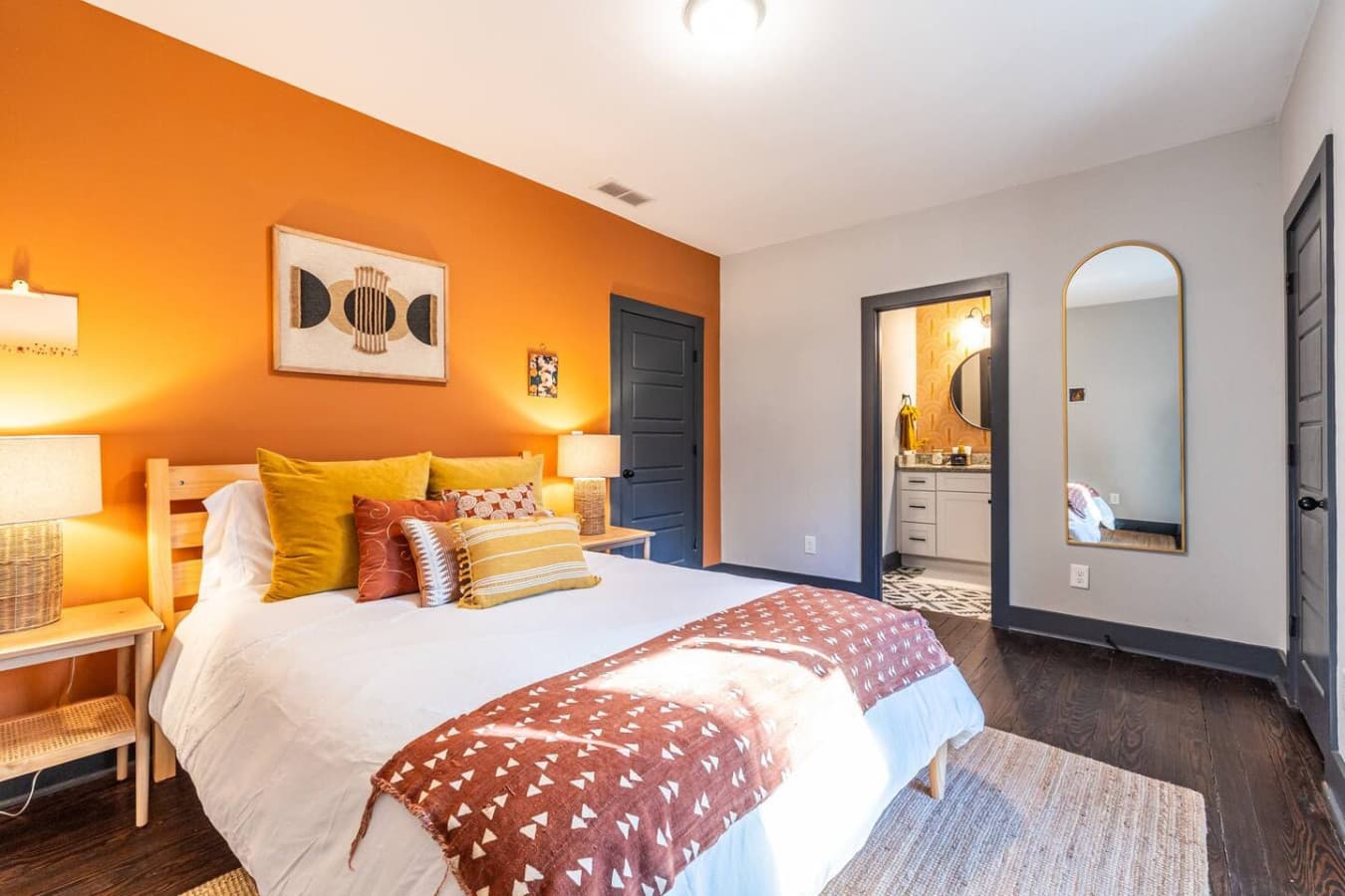 A bright and cheerful guest room with a queen bed, bathed in warm yellows and oranges. A private door provides convenient access to the hall bathroom.