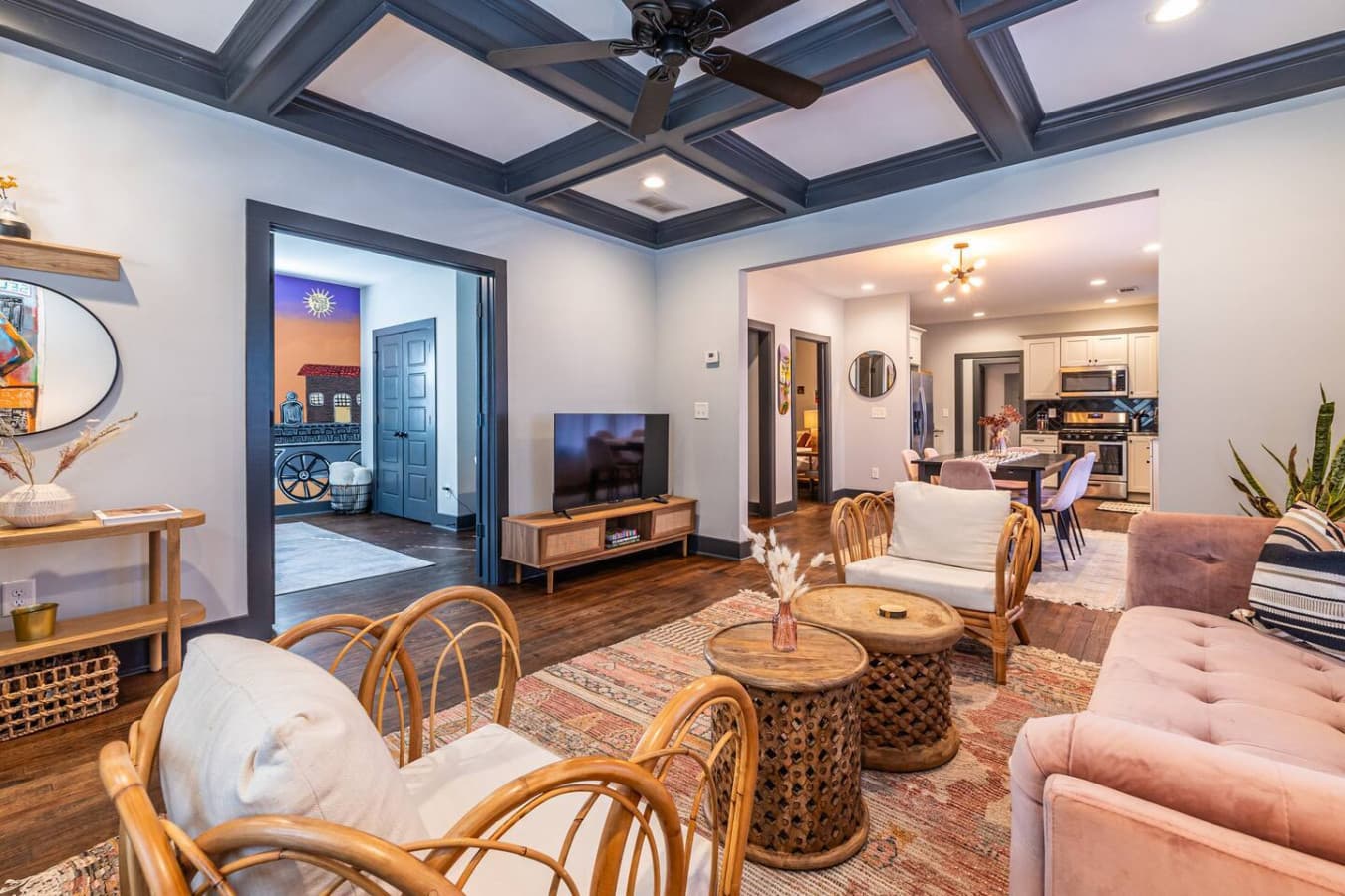 Your stay begins in this inviting, eclectic living room where soft textures, a mauve sofa, and airy rattan details set the tone for a comfortable, stylish retreat that flows easily into the dining and kitchen areas.