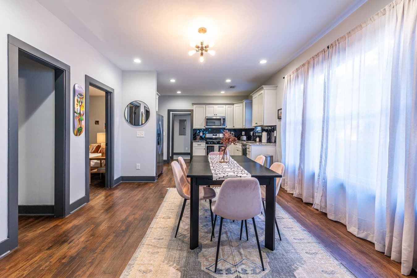 Chic and inviting dining space featuring mauve seating, flowing curtains, and seamless access to the kitchen.