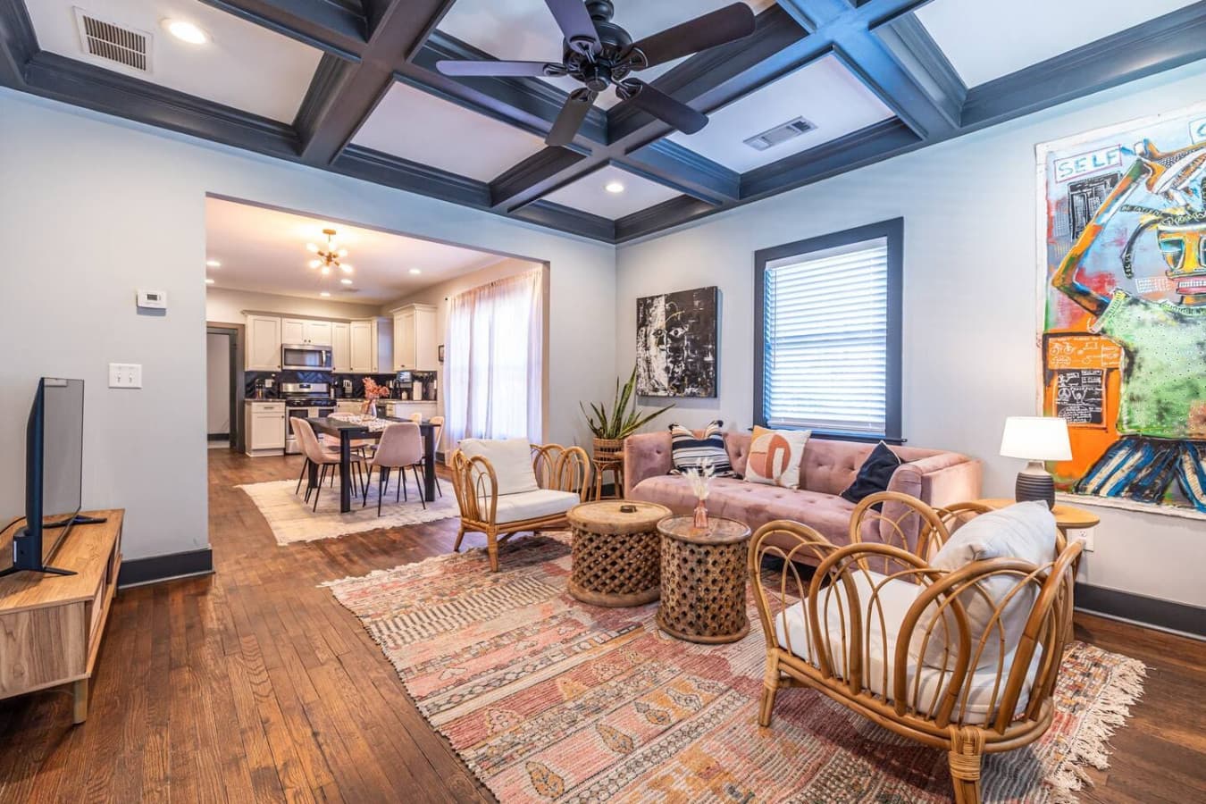 Your stay begins in this inviting, eclectic living room where soft textures, a mauve sofa, and airy rattan details set the tone for a comfortable, stylish retreat that flows easily into the dining and kitchen areas.
