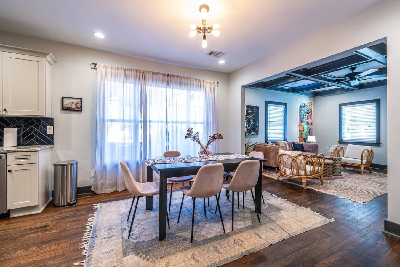 Inviting dining space with comfortable seating and airy drapes, looking out toward the living room, perfect for meals, games, or quality time with loved ones.
