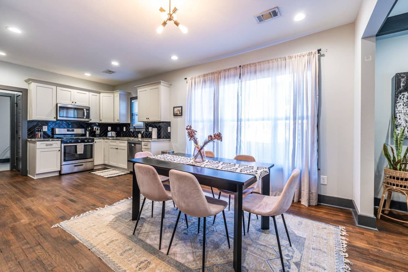 Chic and inviting dining space featuring mauve seating, flowing curtains, and seamless access to the kitchen.