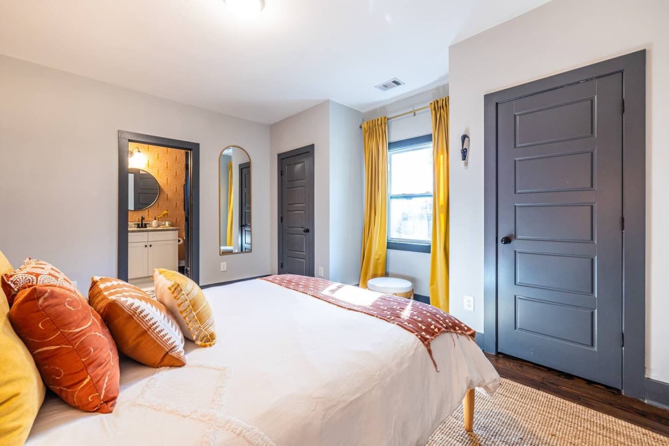 This inviting guest room features a comfortable queen bed surrounded by warm yellows and oranges, creating a cozy atmosphere. Guests enjoy direct access to the hall bathroom through a private door.