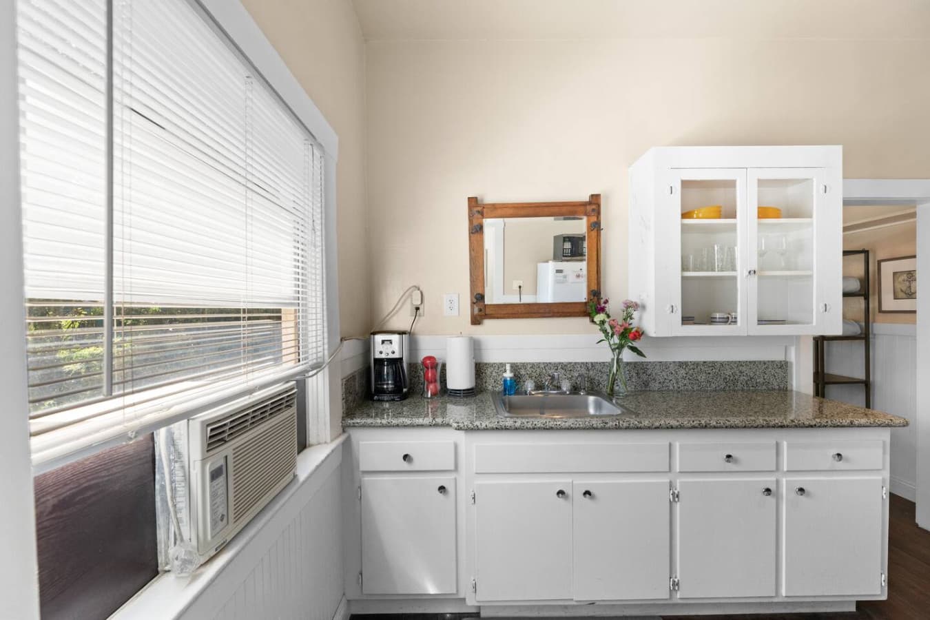 Compact kitchen with granite countertops, white cabinetry, coffee maker, and wall-mounted mirror.