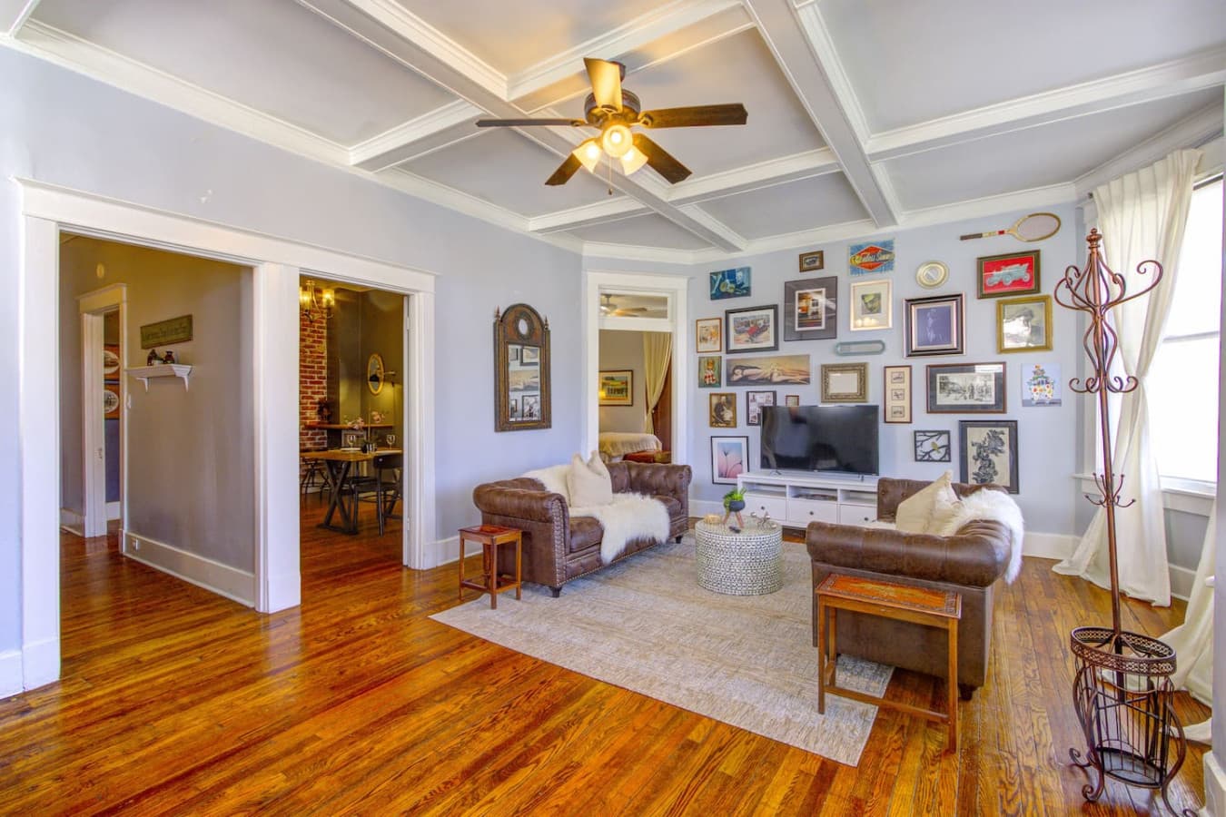Spacious living room with colonial details, coffered ceilings, bay windows, and a curated gallery wall for a touch of historic charm and a smart TV for entertainment.