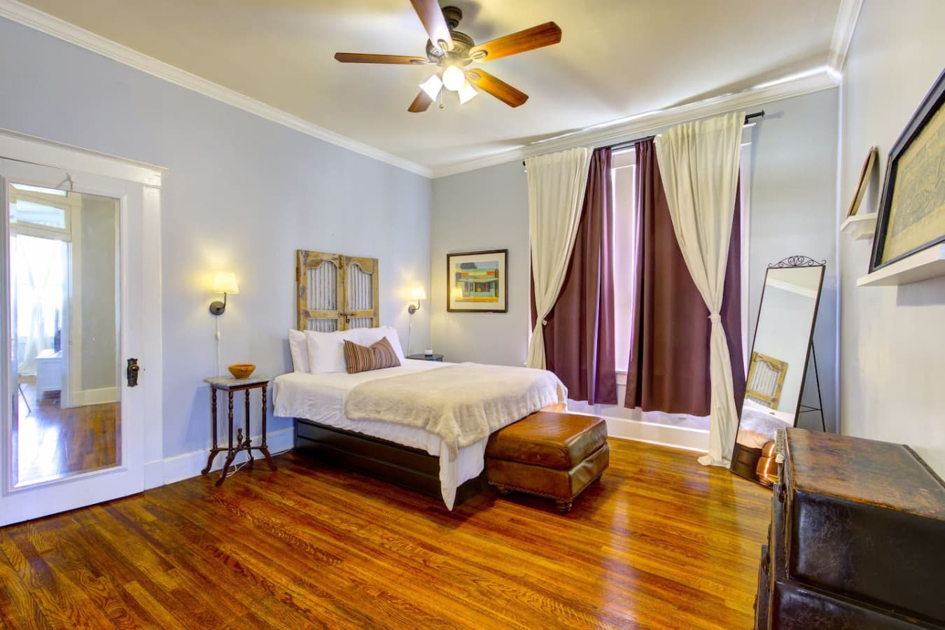 Spacious Bedroom 1 with queen bed, tall windows, and ceiling fan for comfort.