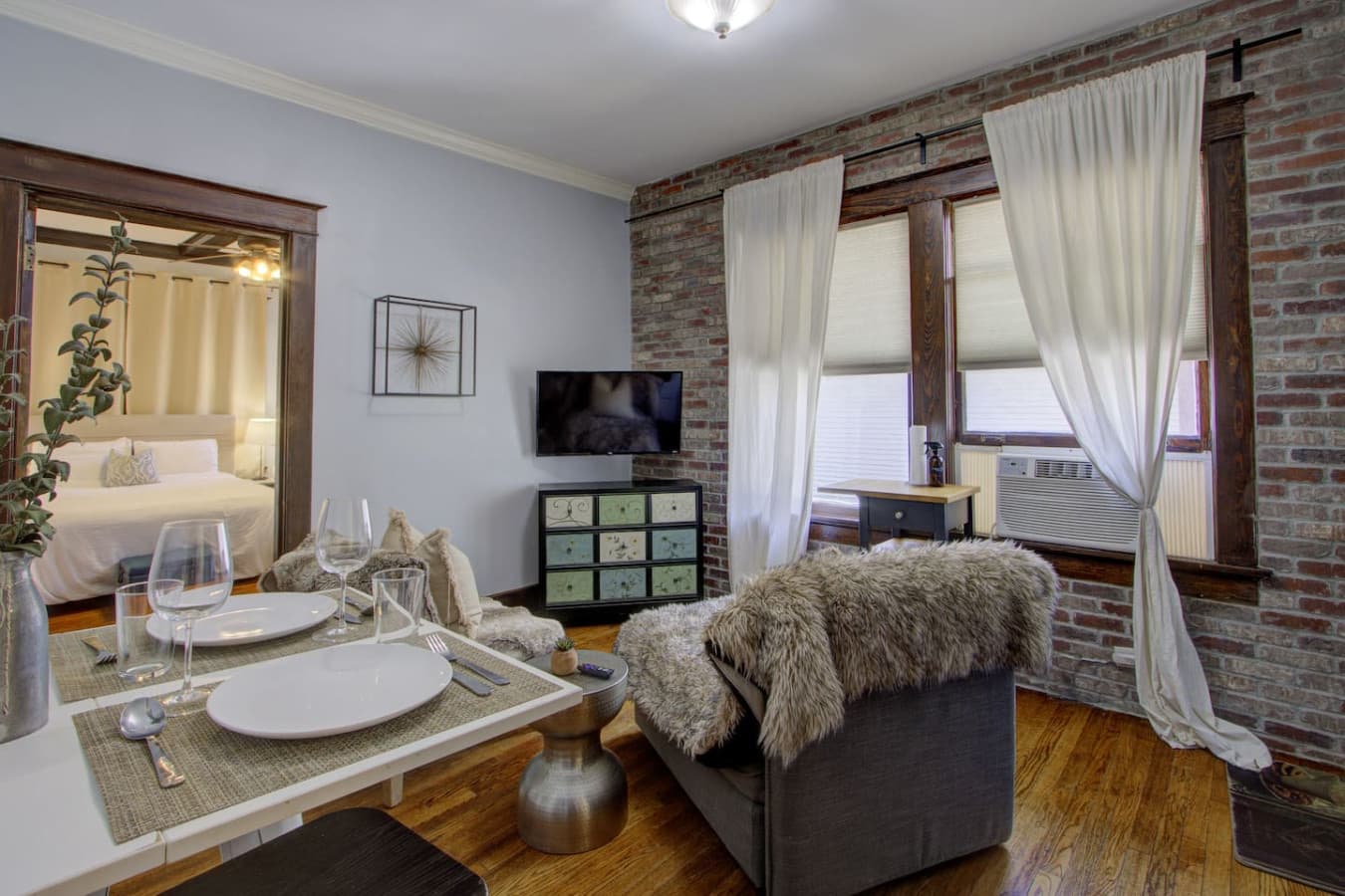 Open view from the living room into the bedroom, featuring exposed brick, natural light, and warm historic details.