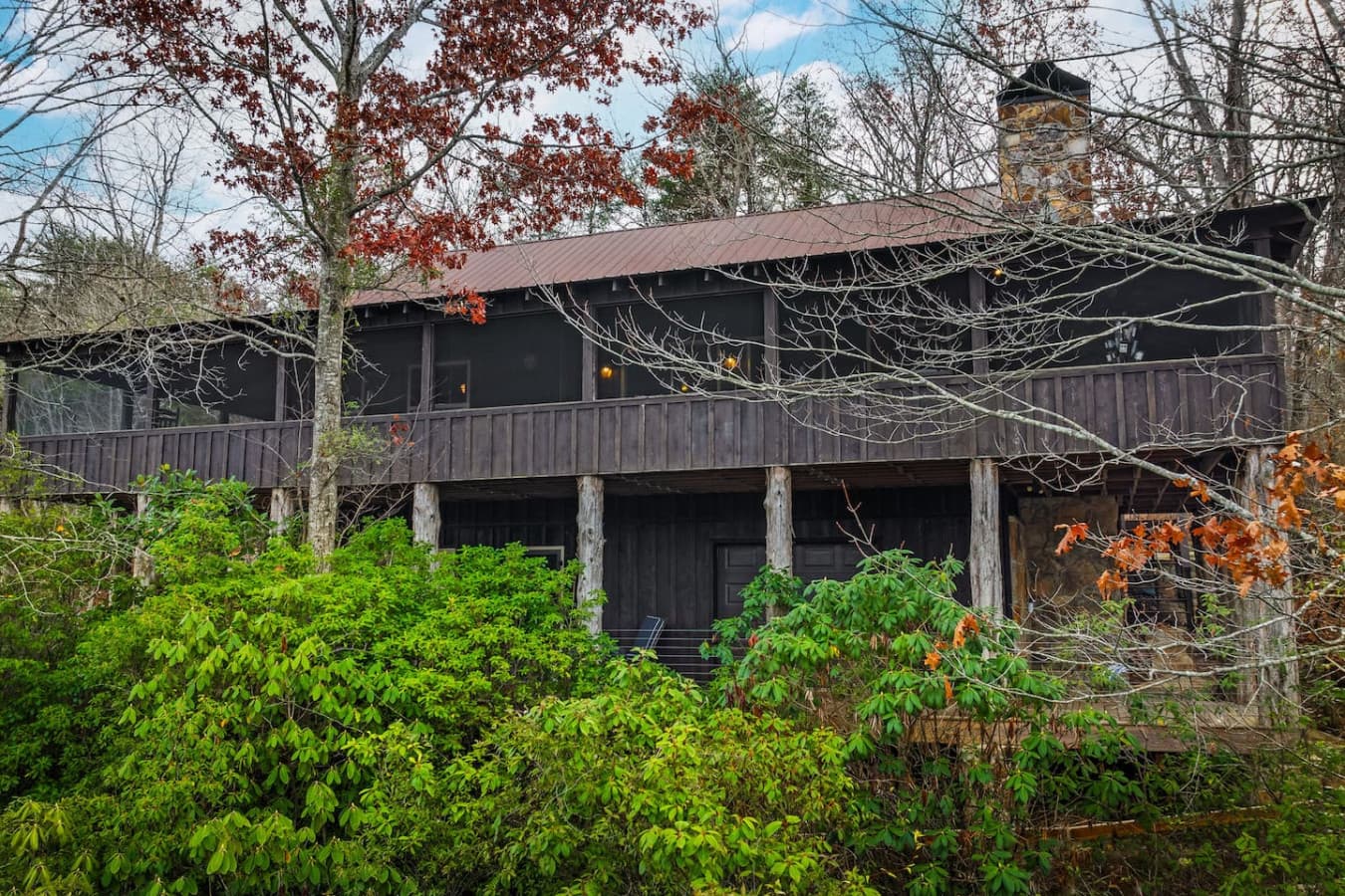 The back porch at Lahusage Landing features an upper screened-in deck with a picnic table, seating, and beautiful views, and a lower deck with seating, an outdoor shower, and a cornhole setup.