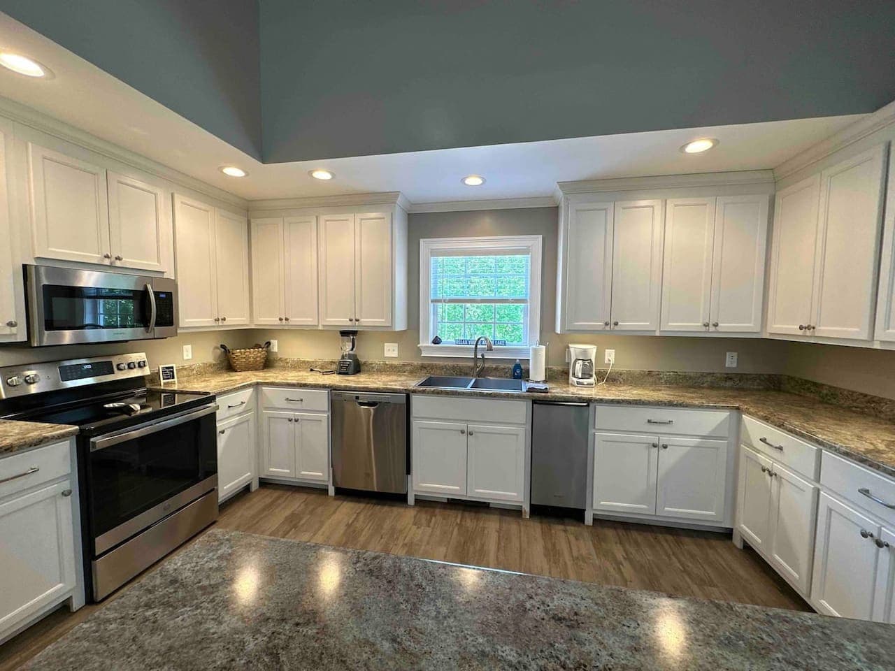 Bright, contemporary kitchen featuring sleek white cabinets, polished stone counters, and a full set of stainless steel appliances. The open layout and wood floors create a warm, inviting cooking space.