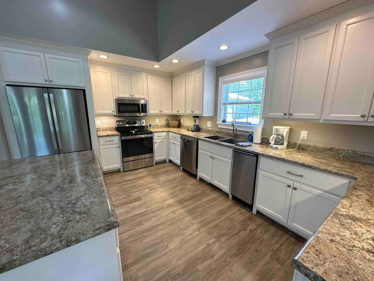 Elegant kitchen with a functional U-shaped layout, highlighted by granite surfaces, modern fixtures, and under-cabinet lighting. The window-centered sink and neutral tones give the space an airy, refined feel.