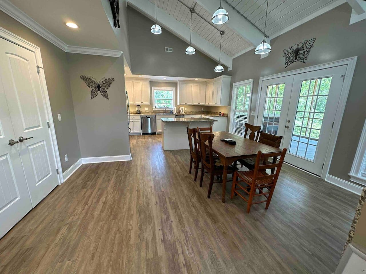 Open dining area with vaulted ceilings and natural light from large glass doors leading to the deck. Features a wooden dining table for six and decorative wall art, creating a bright and welcoming space for gatherings.