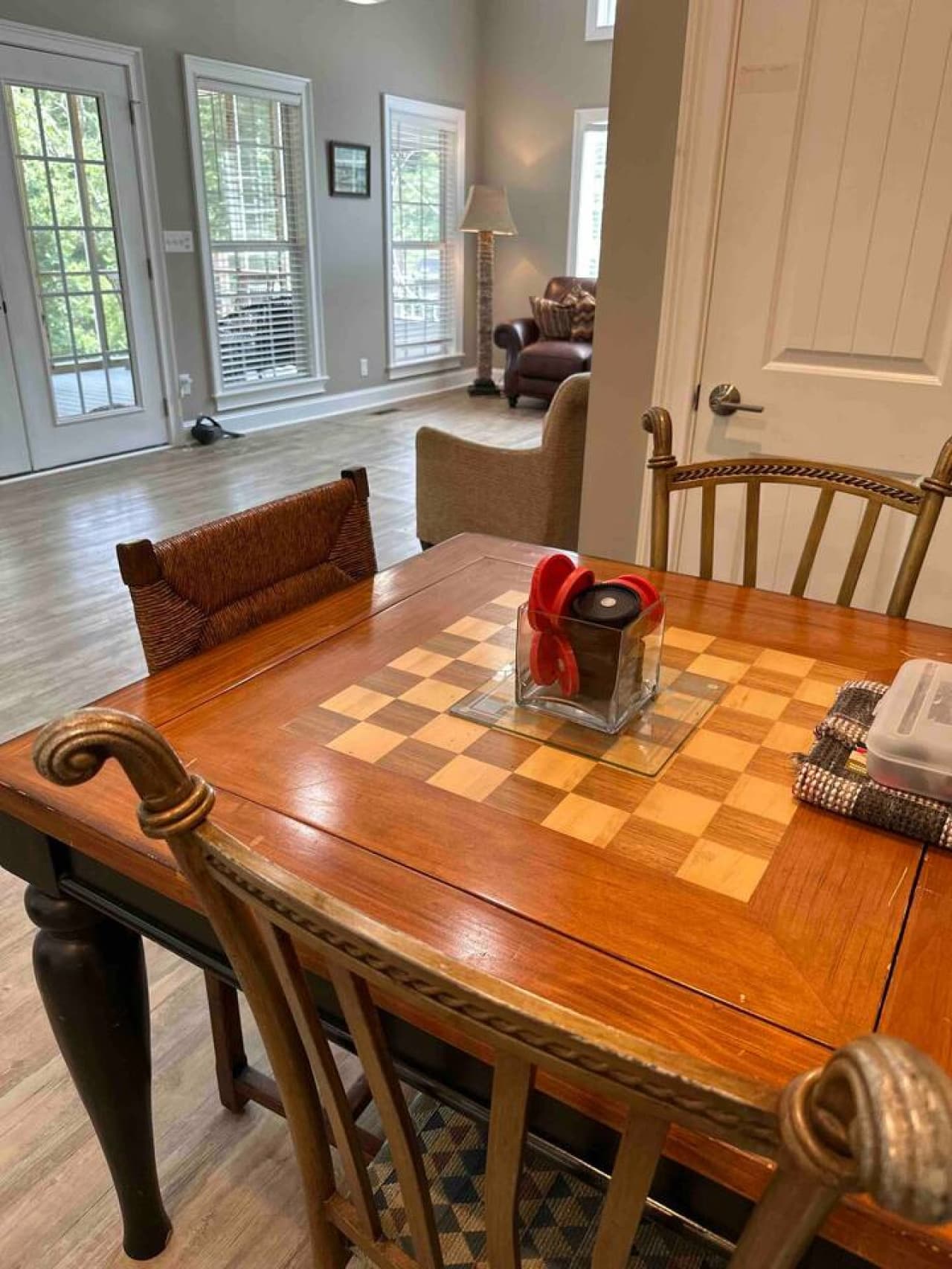 Game table in the living room featuring a checkered design, surrounded by chairs and overlooking a bright seating area with large windows and patio access.