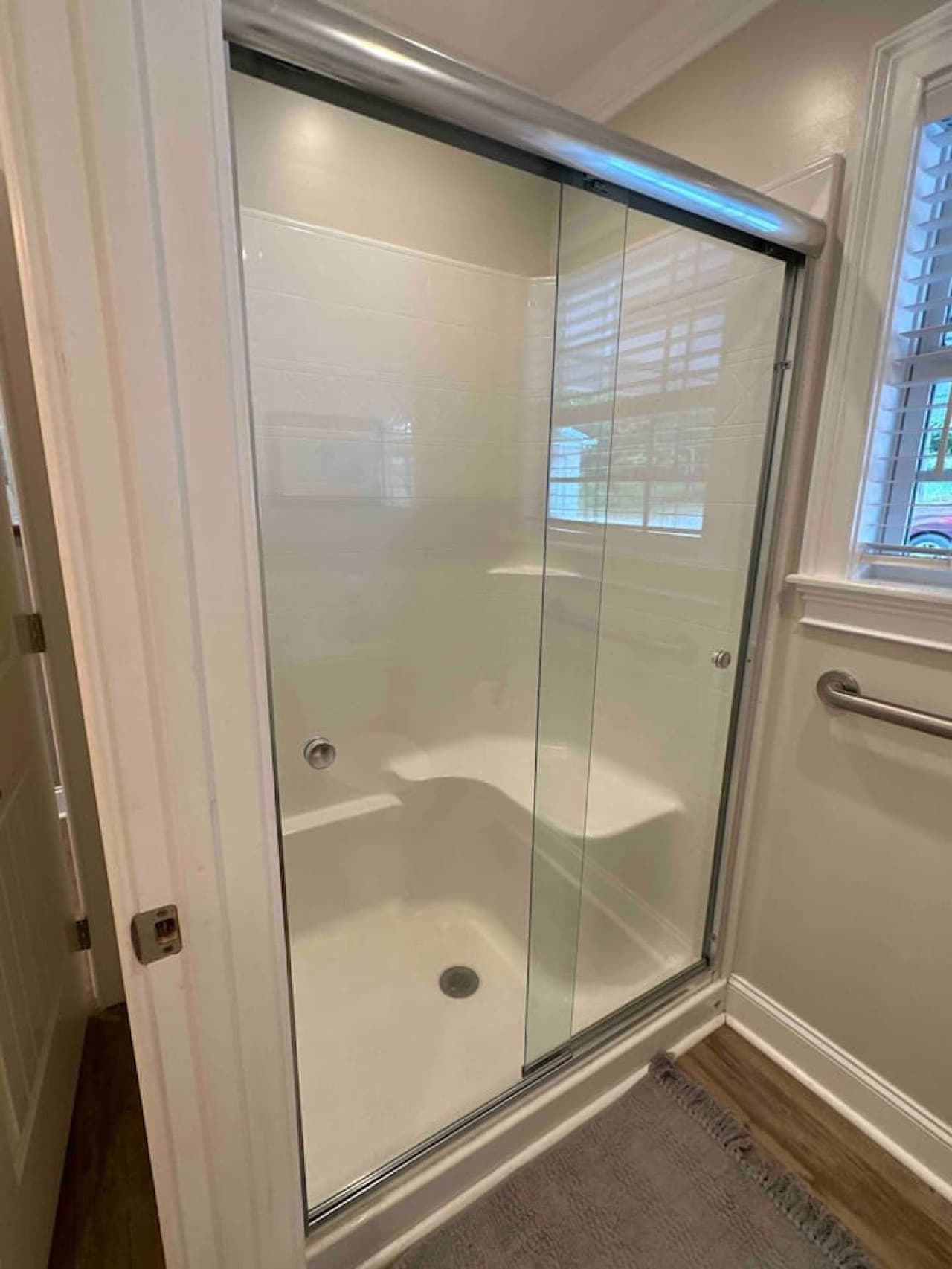Bright, modern shower with glass sliding doors and built-in bench seating. Features clean tile walls, chrome fixtures, and natural light from a nearby window.
