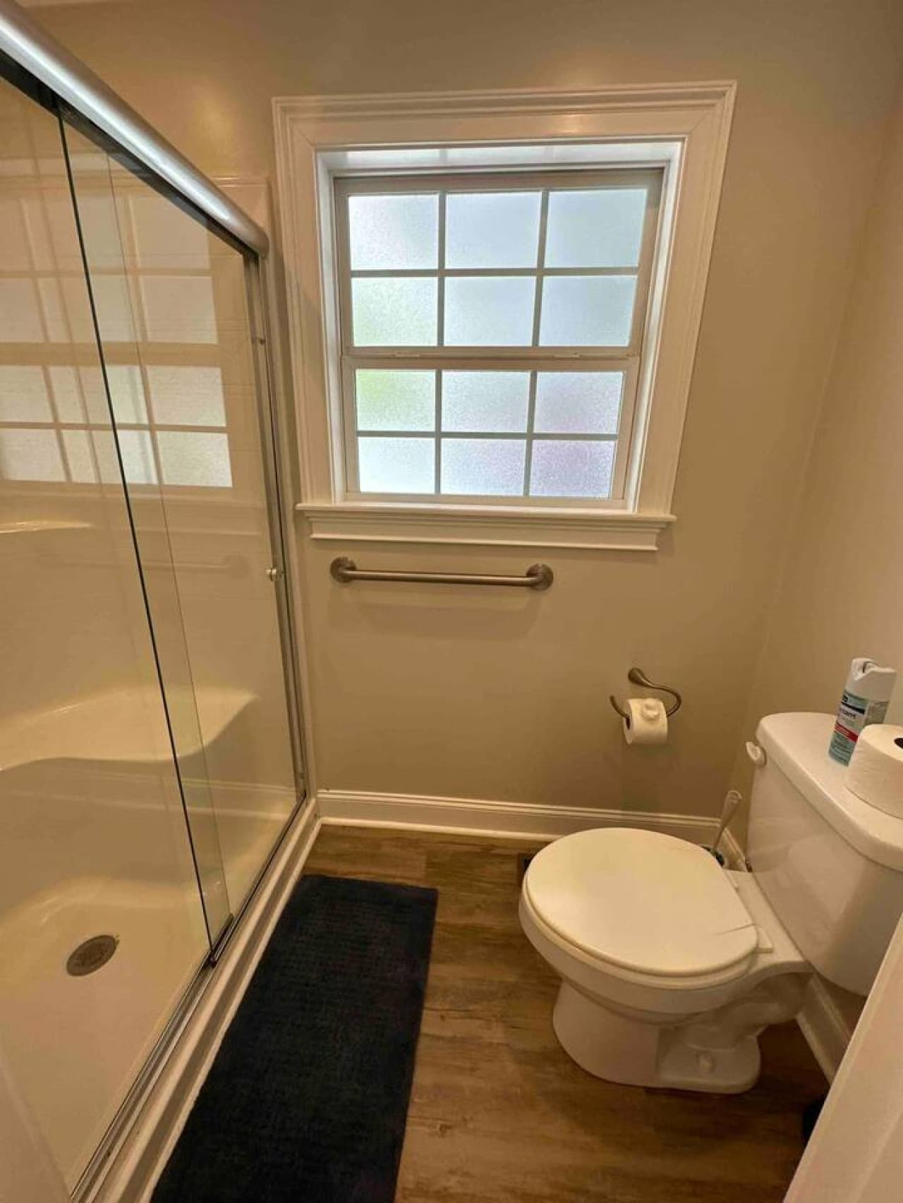Clean, modern bathroom with a glass-enclosed shower, toilet, and natural light from a large window.