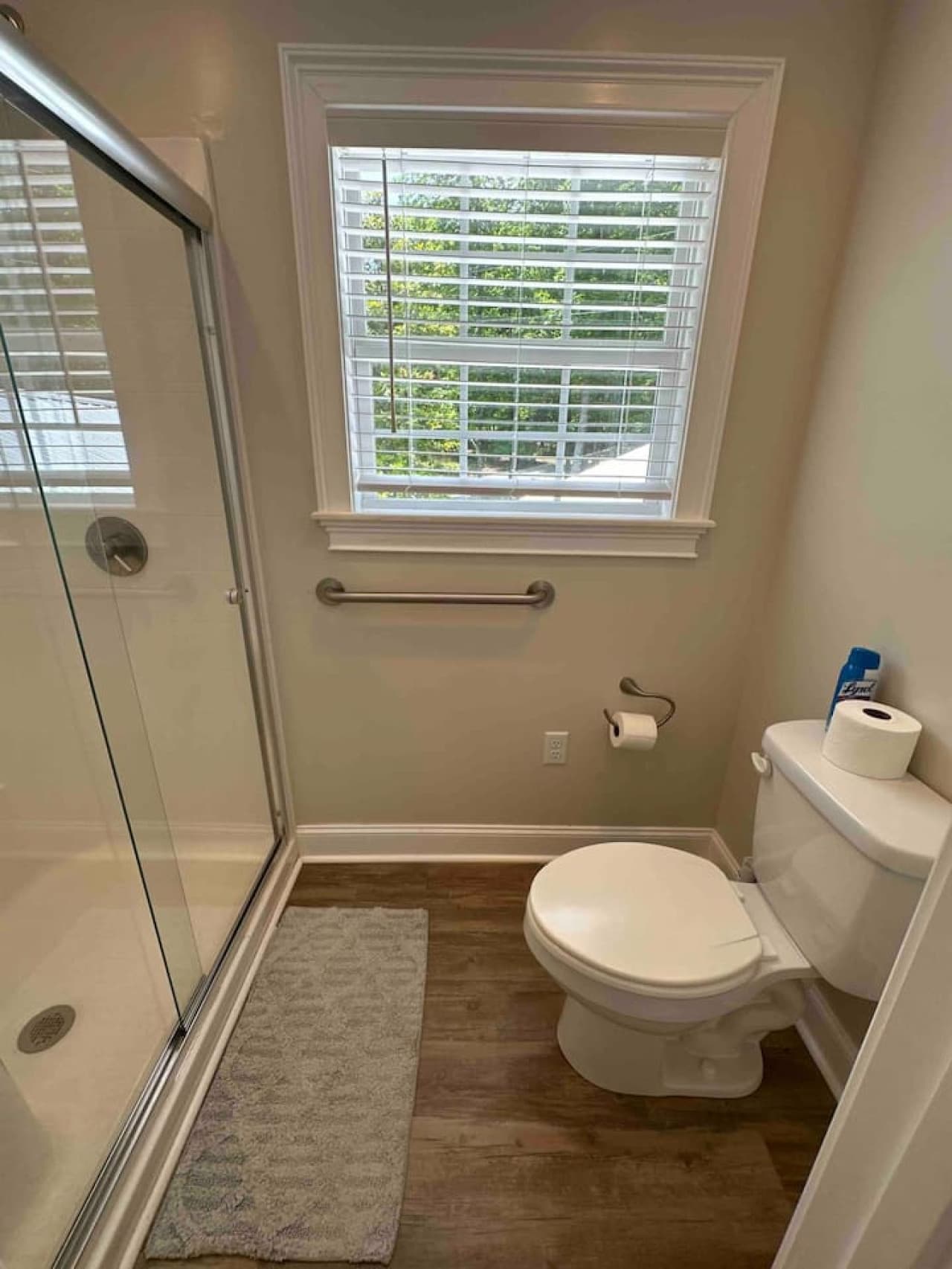 Clean, modern bathroom with a glass-enclosed shower, toilet, and natural light from a large window.
