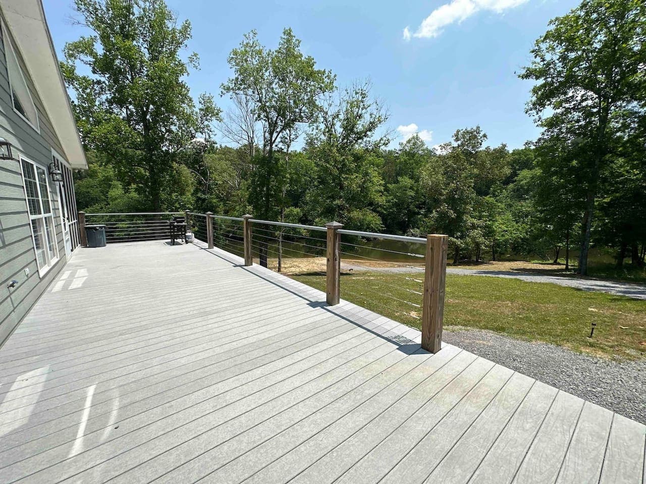 Expansive front deck with modern cable railing, offering scenic views of the surrounding trees and river—perfect for outdoor relaxation or grilling.