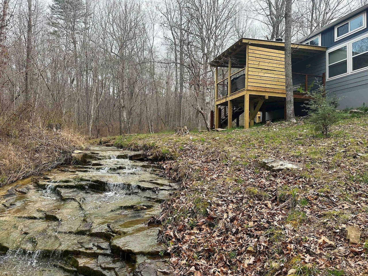 The Whimsical Waterfall Cottage features a newly added hot tub deck overlooking the creek and waterfall, along with a charcoal grill for outdoor cooking.