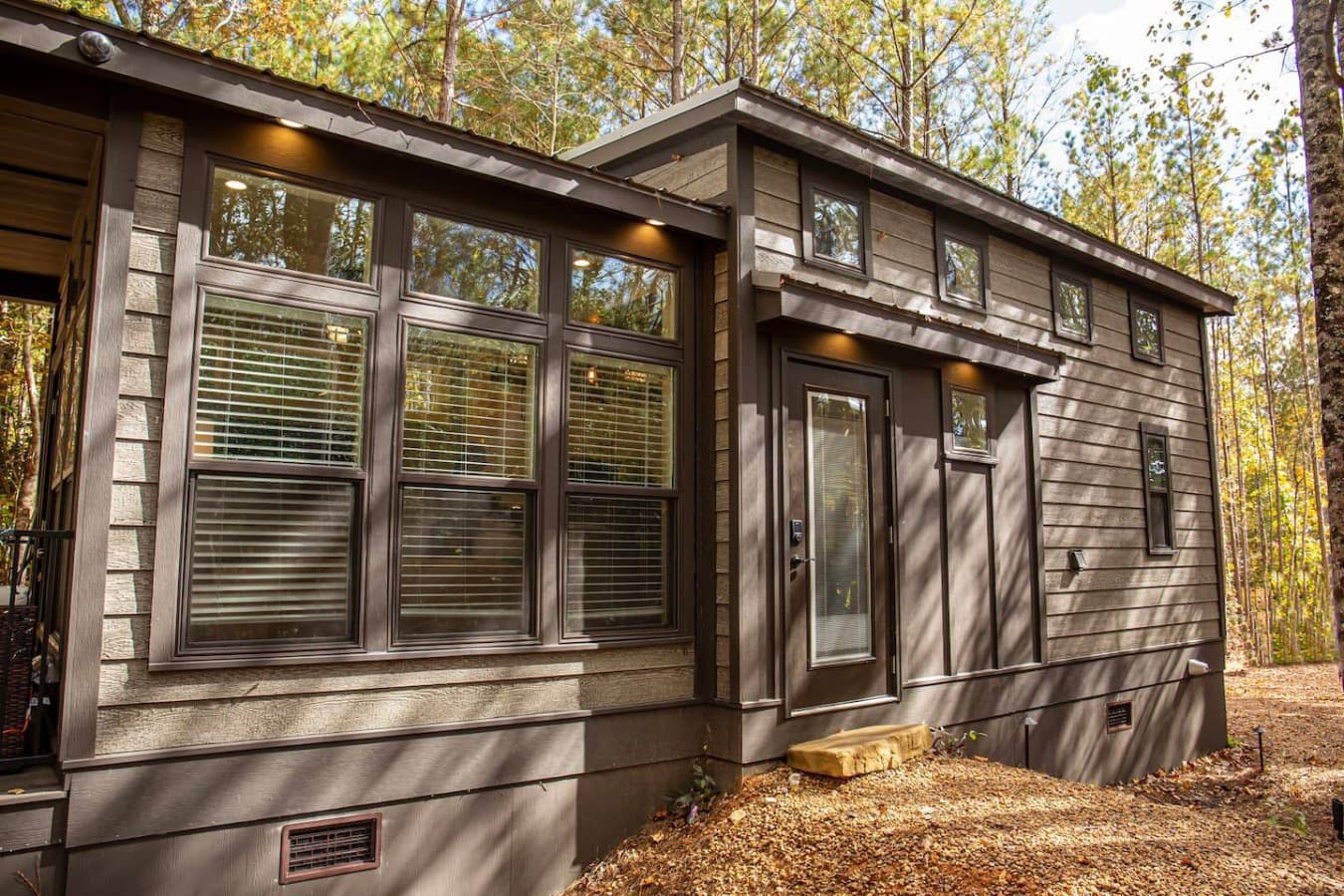 This charming tiny home, nestled in the woods, features a sleek and modern exterior with large windows that let in plenty of natural light.