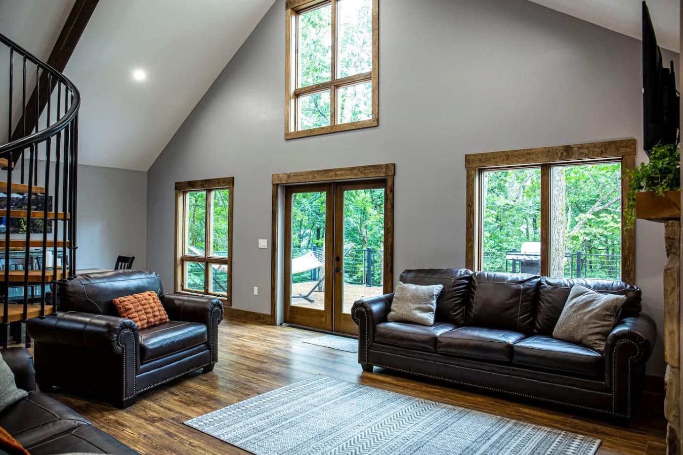 Bright and spacious living room with leather seating, vaulted ceilings, and large windows offering serene forest views.
