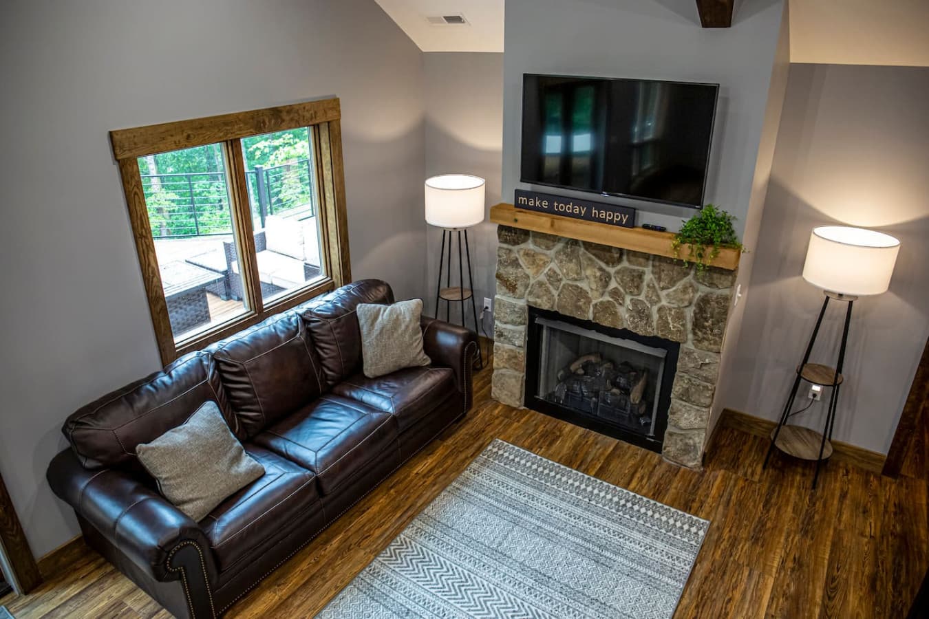 Living room with a stone gas fireplace, smart TV, and leather sofa overlooking the forest-view deck.