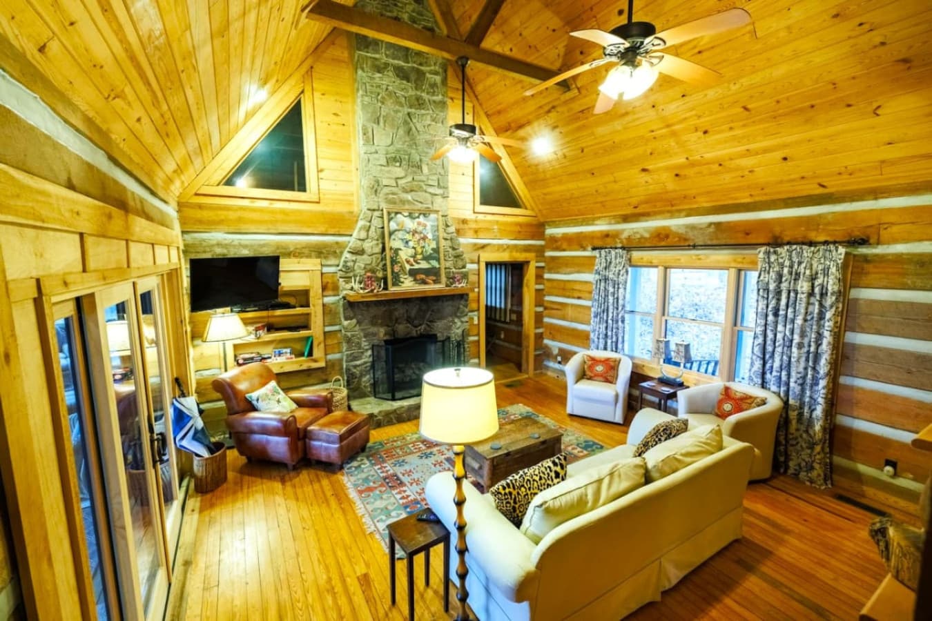 Cozy up in the heart of the cabin, a warm, wood-paneled living room with plush seating, soft throws, and a stone fireplace that invites you to unwind after a day outdoors.