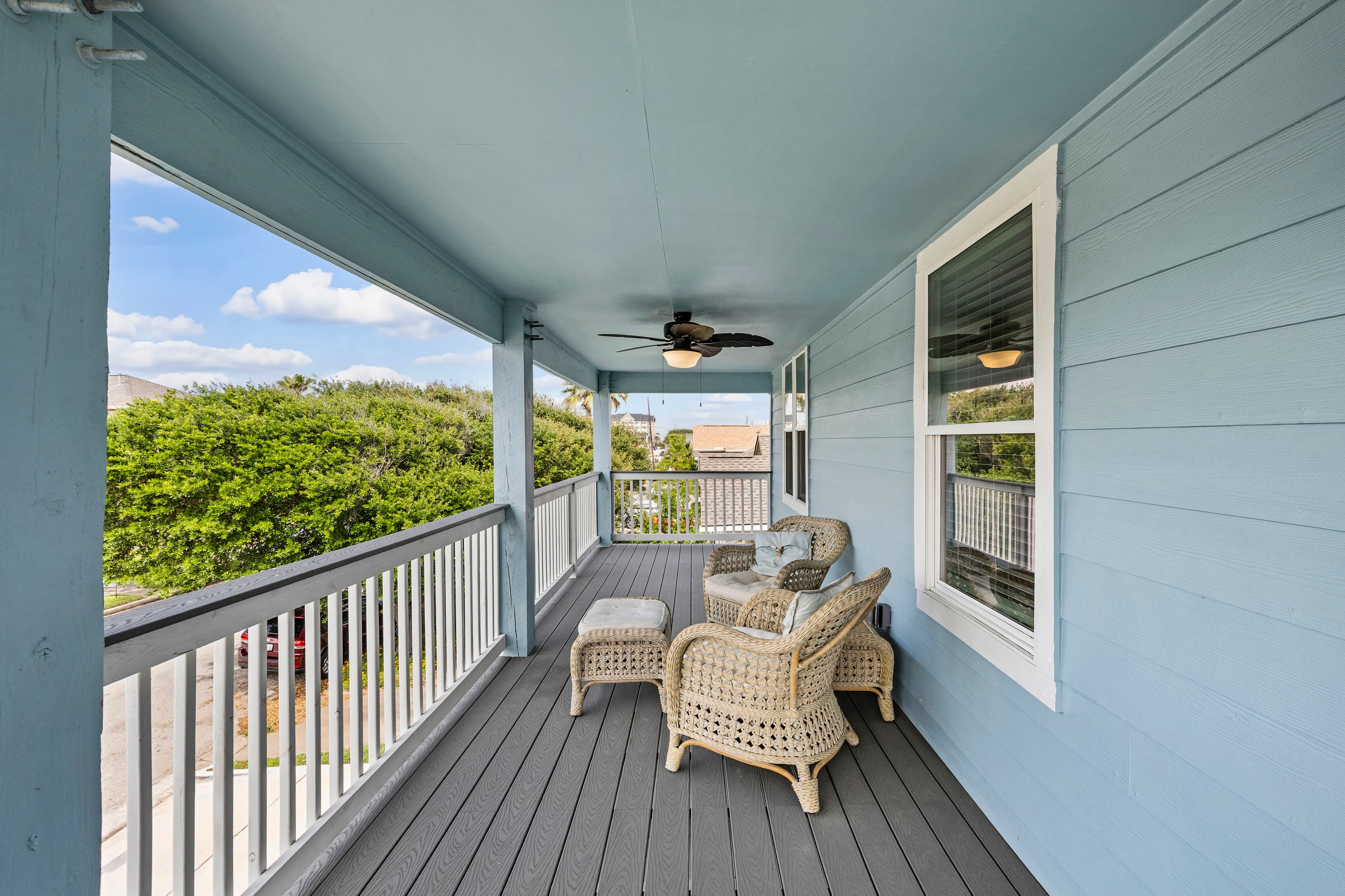 Wraparound deck lounge at The Lookout at R½ — wicker chairs, a ceiling fan for warm Galveston days, and tropical greenery just beyond the railing. Step outside and unwind.