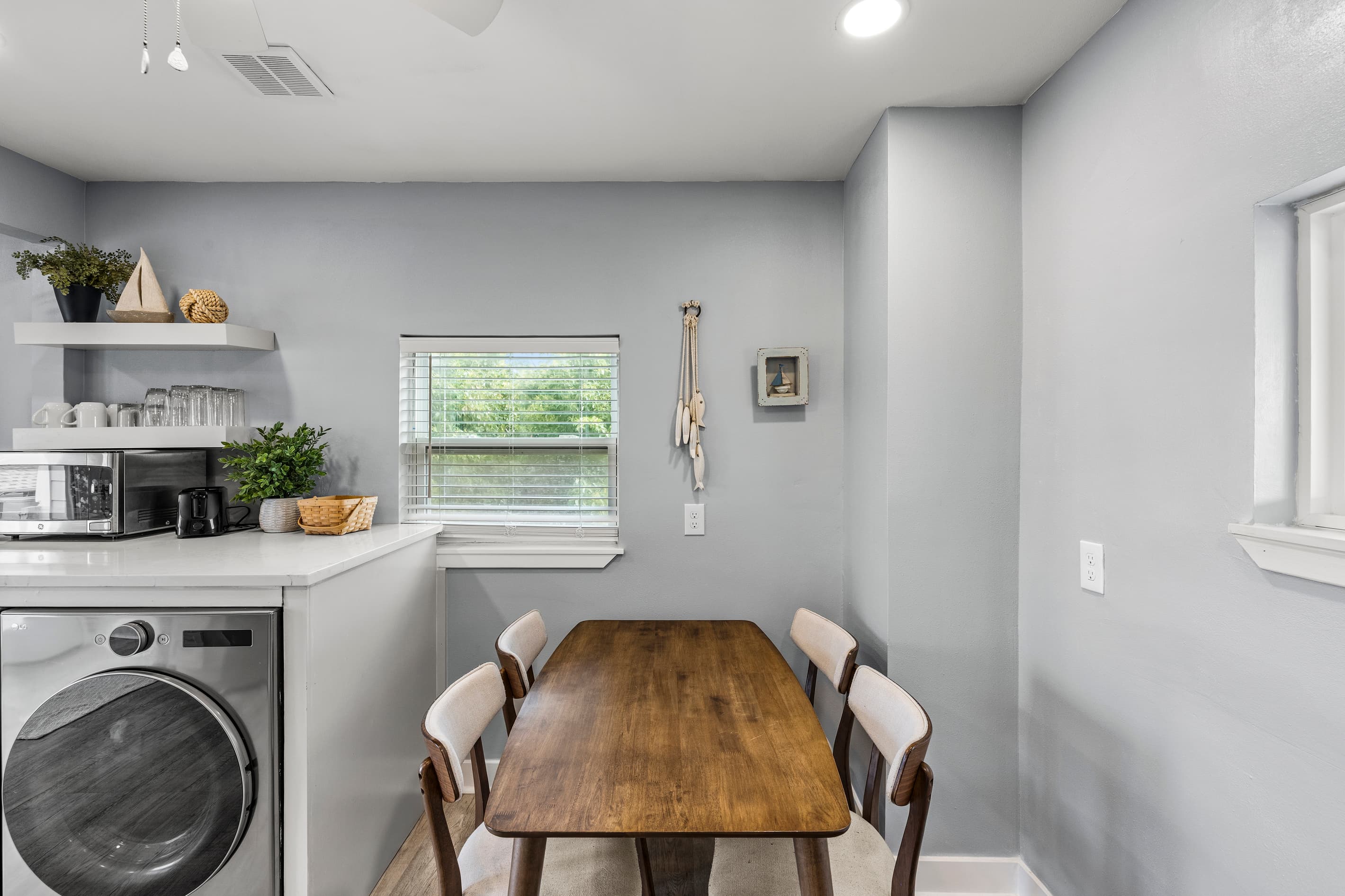 Dining area at The Lookout at R½ — a solid wood table for four, coffee station with open shelving, in-unit washer, and a bright window with neighborhood views.