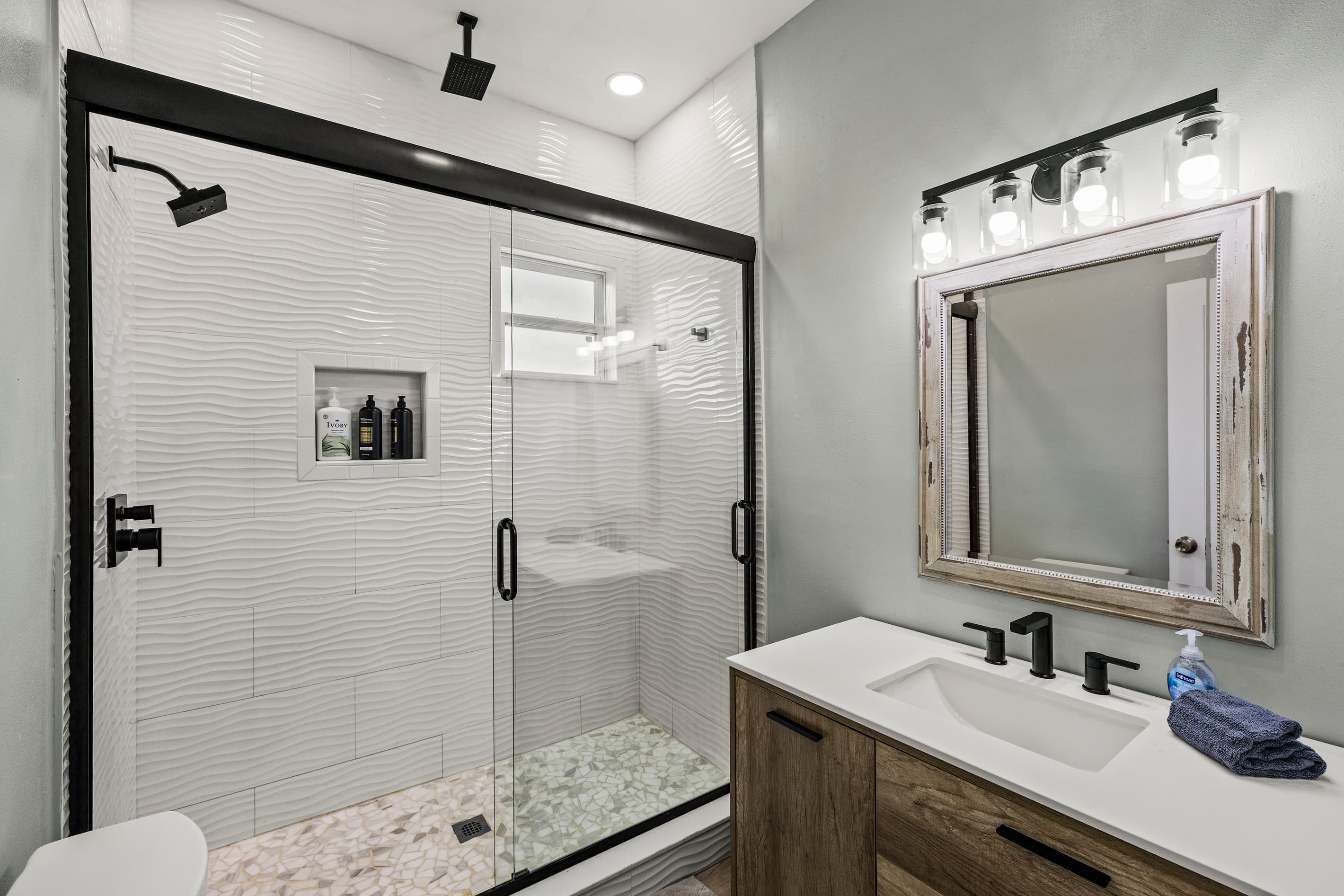 The bathroom at The Lookout at R½ — glass-enclosed walk-in shower with white tile, matte black fixtures, wood vanity, and Hollywood vanity lighting. Spa-quality finish.