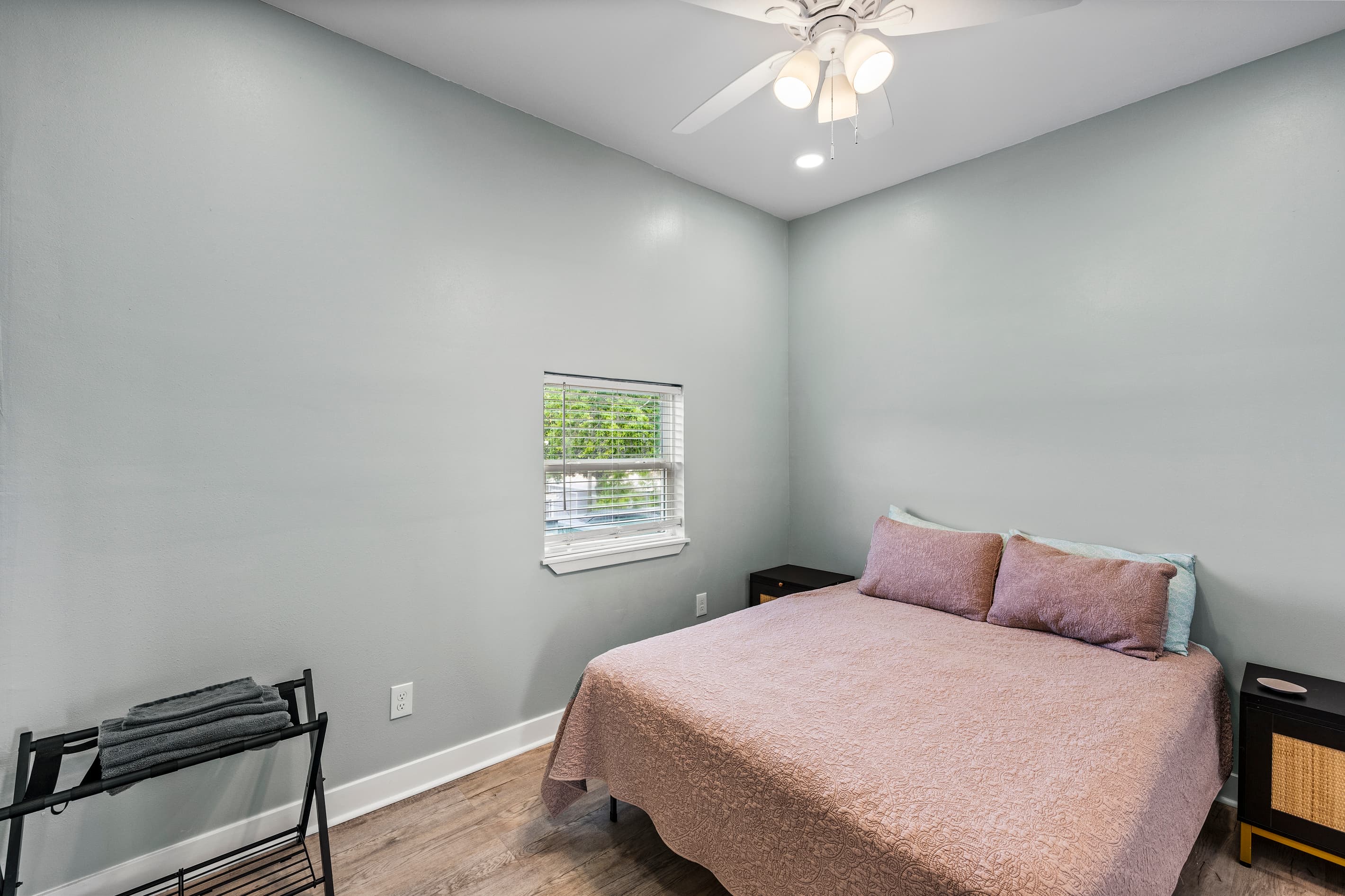 Bedroom 2 at The Lookout at R½ — a cozy second bedroom with ceiling fan, luggage rack, and a garden-view window. Perfect for kids or additional guests.