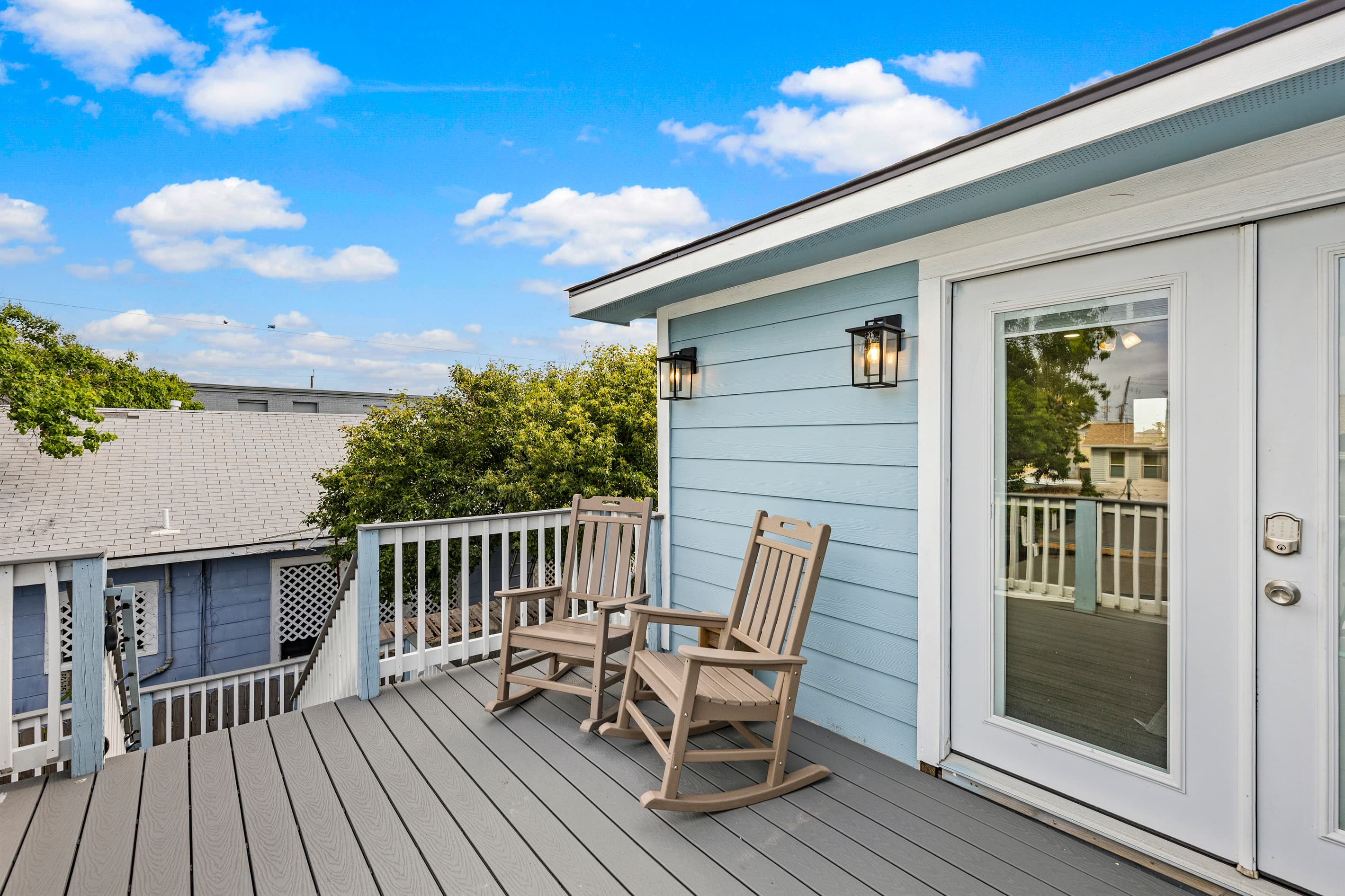 The upper wraparound deck at The Lookout at R½ — a private rocking chair, lush greenery, and a French door entry. Your own elevated retreat above the Galveston Seawall.