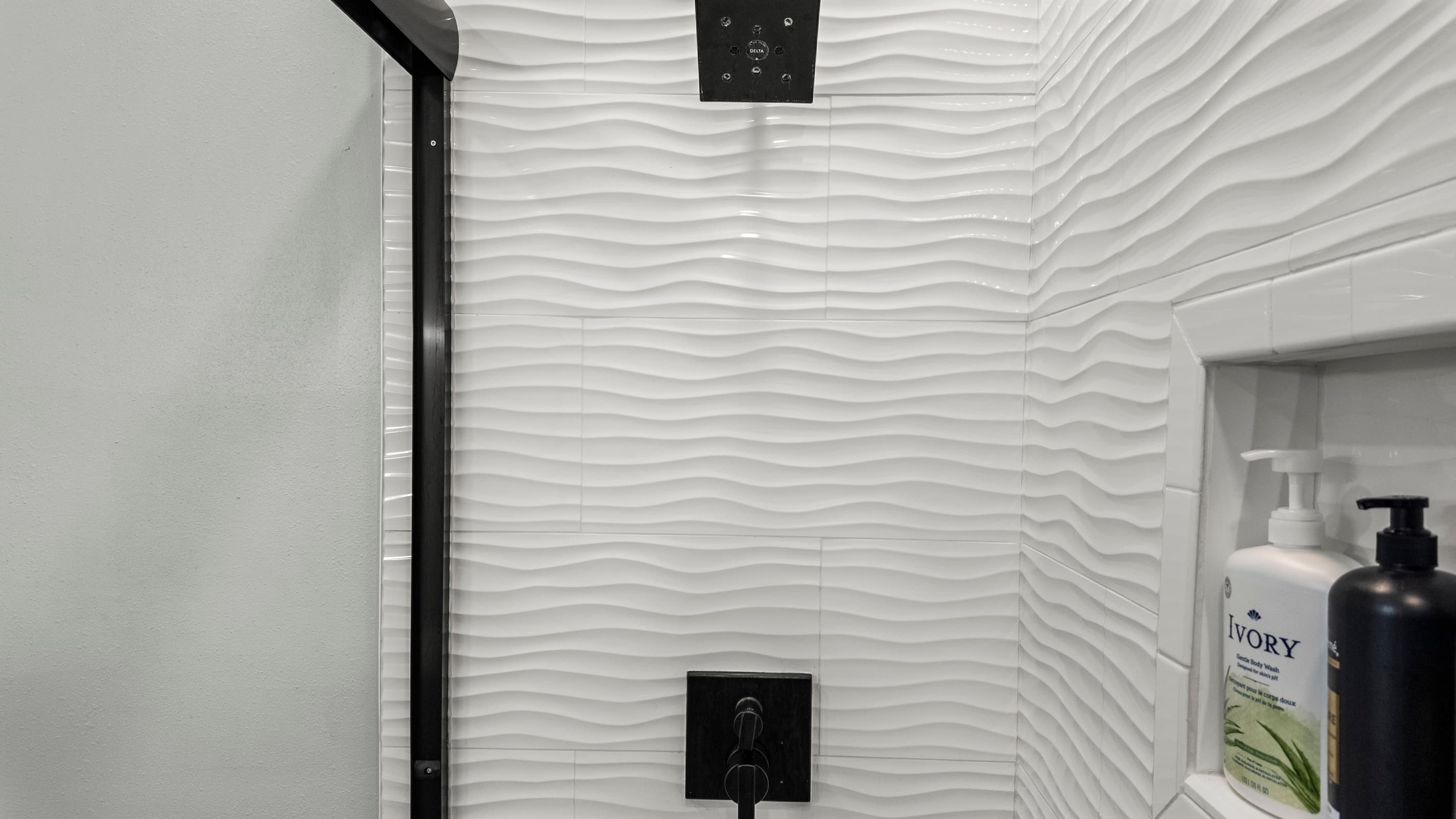 The walk-in shower at The Lookout at R½ — textured wave tile, matte black fixtures, and a built-in niche stocked with shampoo, conditioner, and body wash. No packing required.