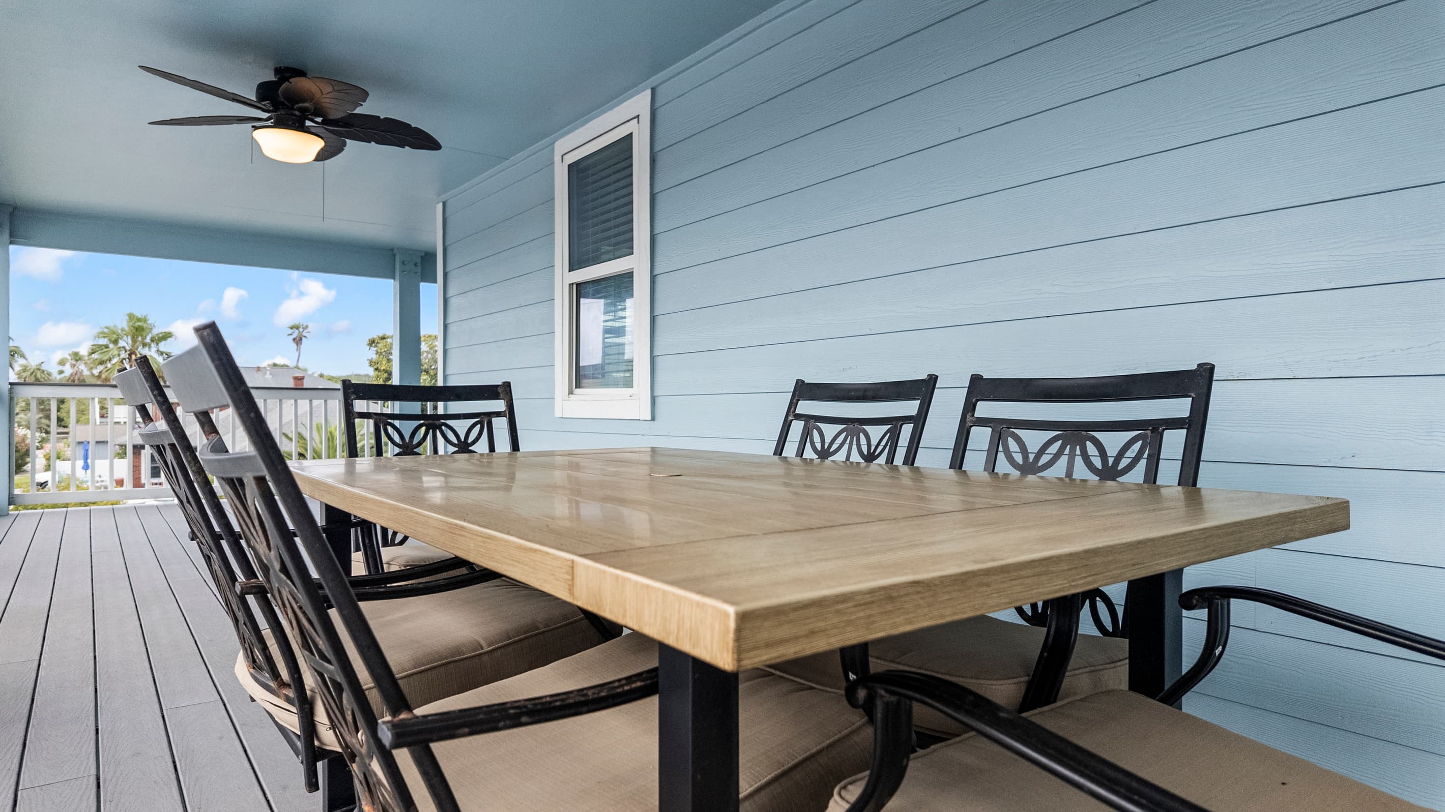 Outdoor dining on the wraparound deck at The Lookout at R½ — a full table for six, ceiling fan overhead, and Gulf views and palm trees framing every meal.