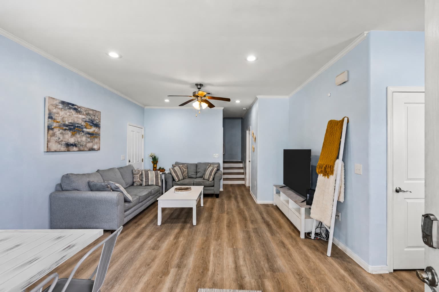 The living room at Summer Bliss — light blue walls, comfortable sofa, and coastal wall art. Hardwood floors and a ceiling fan keep things cool after beach days.