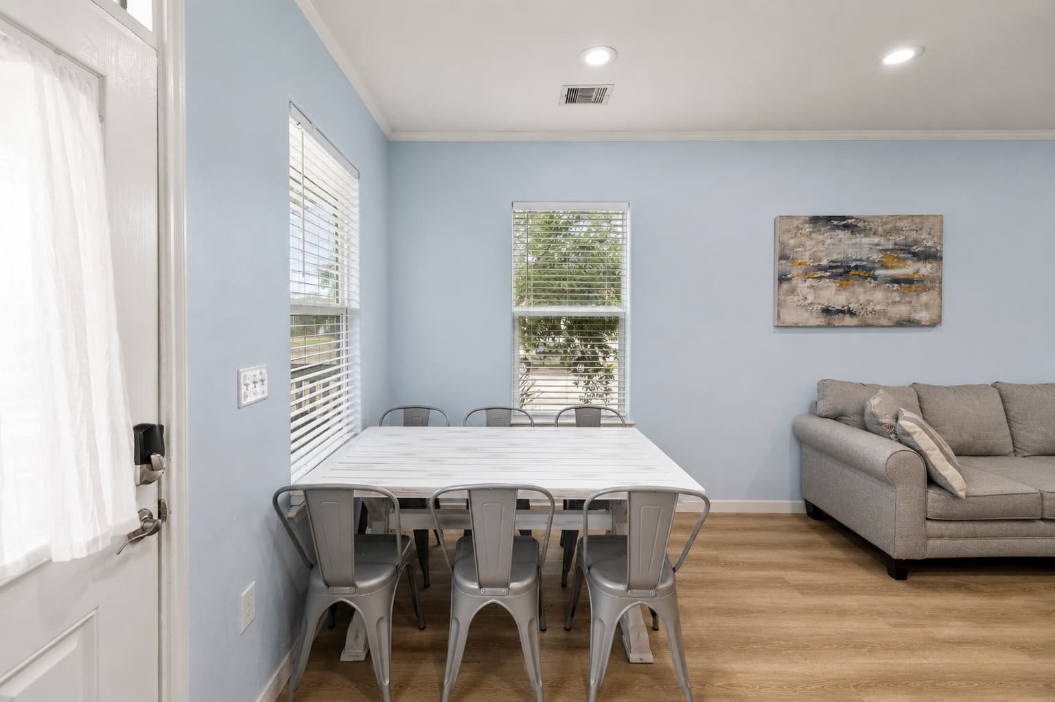 The dining area at Summer Bliss — a white table with metal chairs for the whole group, natural light from the window, and easy flow to the kitchen. Everyone eats together.