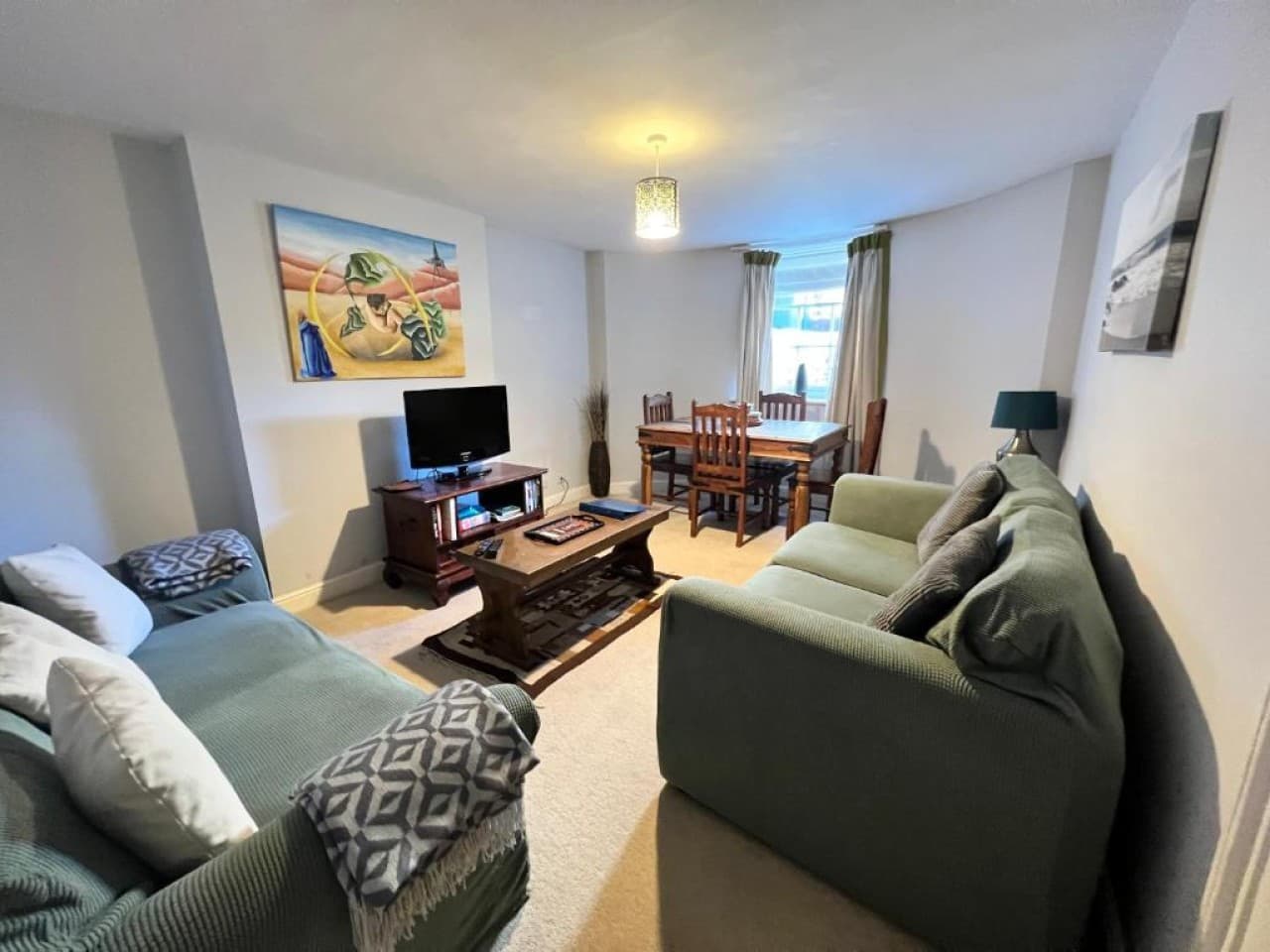 Open-plan living/dining - green sofas, dining table, flat-screen TV (angle 1)