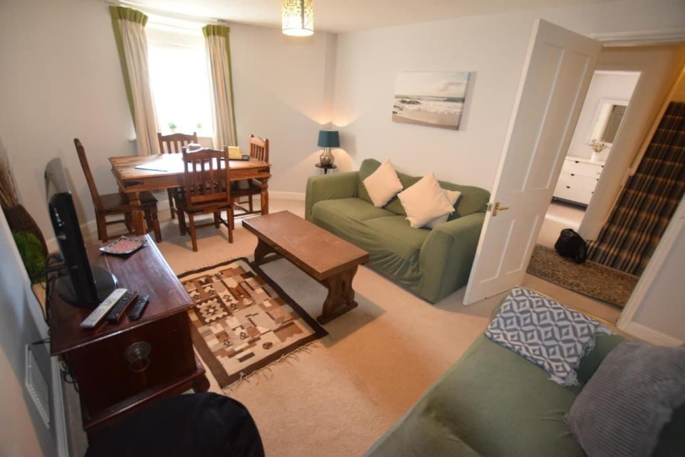 Open-plan living/dining - green sofa, TV cabinet, dining table, area rugs (angle 2)