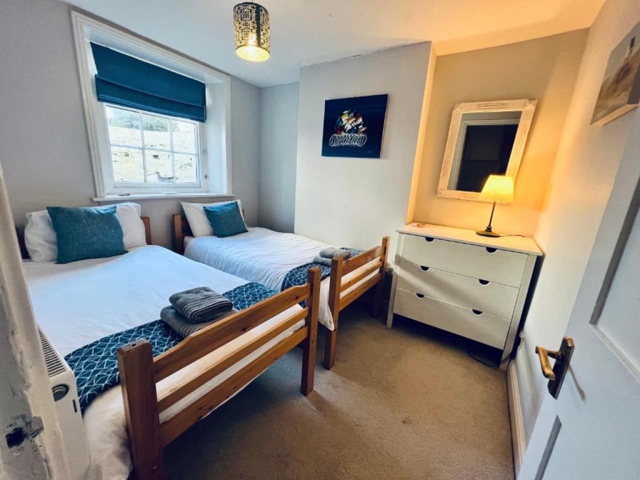 Bedroom 2 - twin beds, teal cushions, dresser with mirror, hillside view (angle 1)