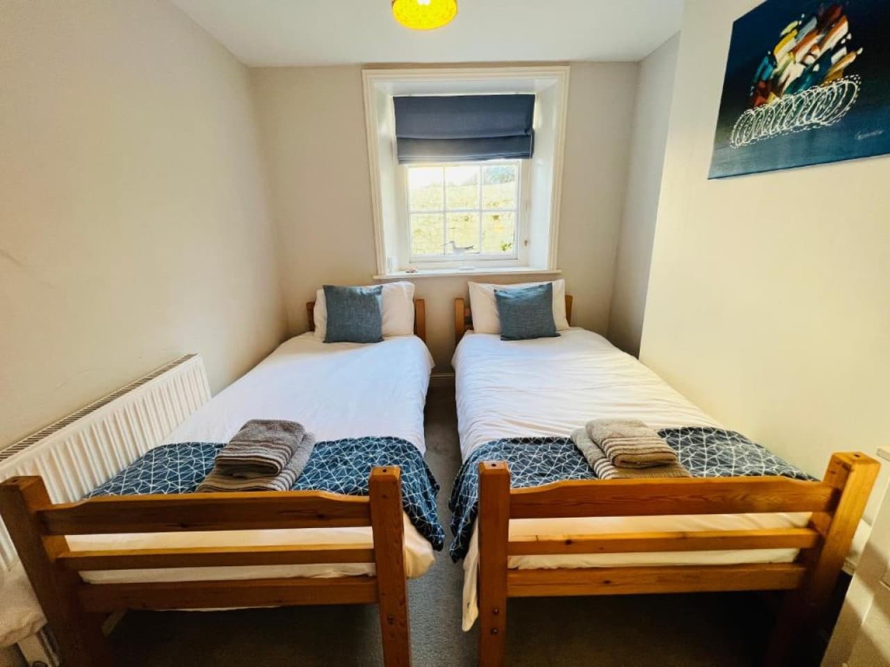 Bedroom 2 - twin beds, patterned throws, radiator, Roman blind (angle 2)