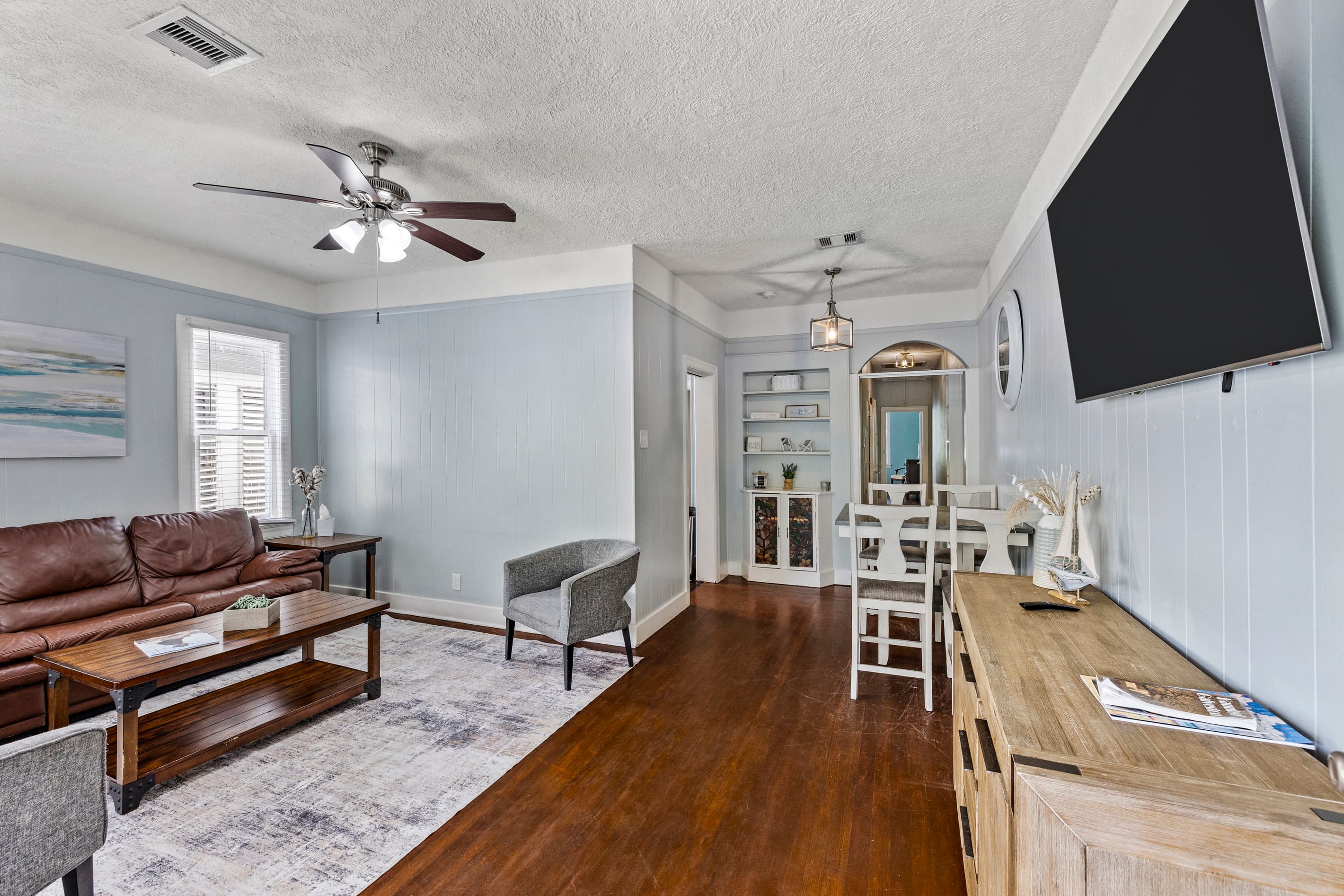 Step inside Port Side at M and settle in — a bright, comfortable living room with a leather sofa, original hardwood floors, and the easy warmth of a renovated Galveston classic.