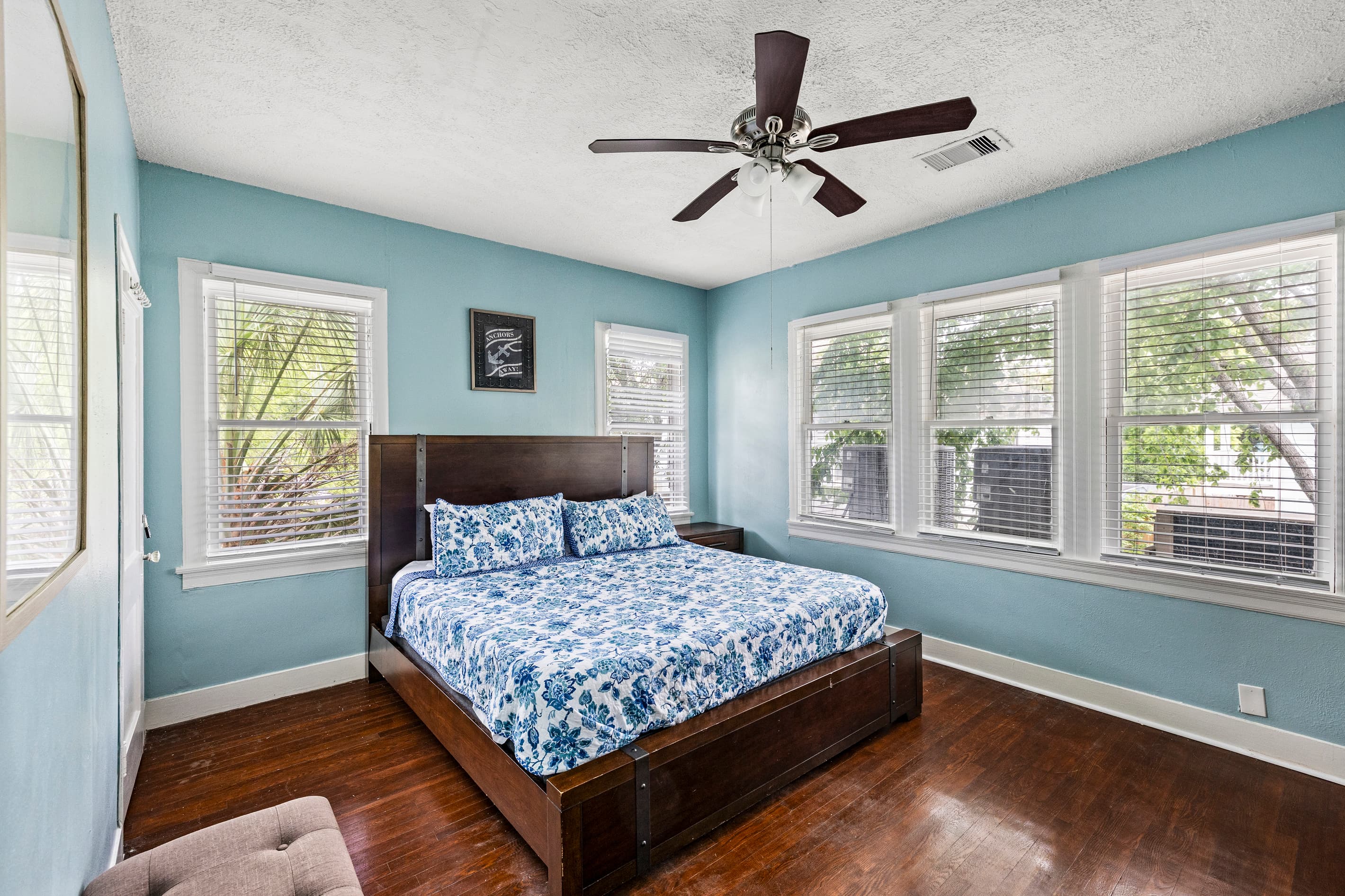 The primary bedroom at Port Side at M features a comfortable king bed, a ceiling fan, and bright windows — restful nights in historic Lost Bayou.