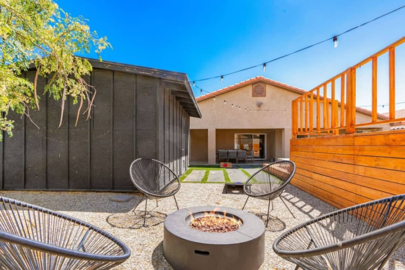 Inviting courtyard w/ modern firepit seating, gravel patio, & string lights for relaxed evenings outdoors.